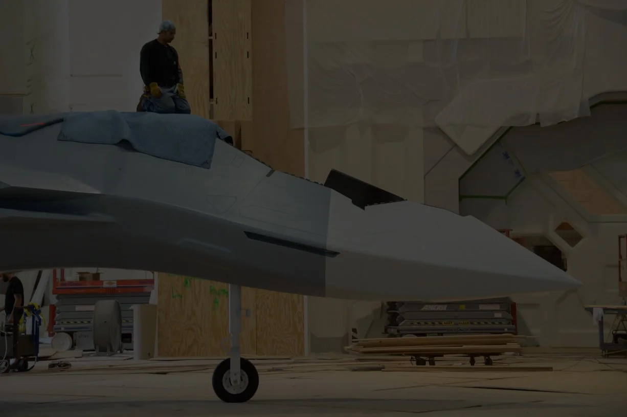 A person in a factory working on a fighter jet inside a workshop with tools and equipment around.