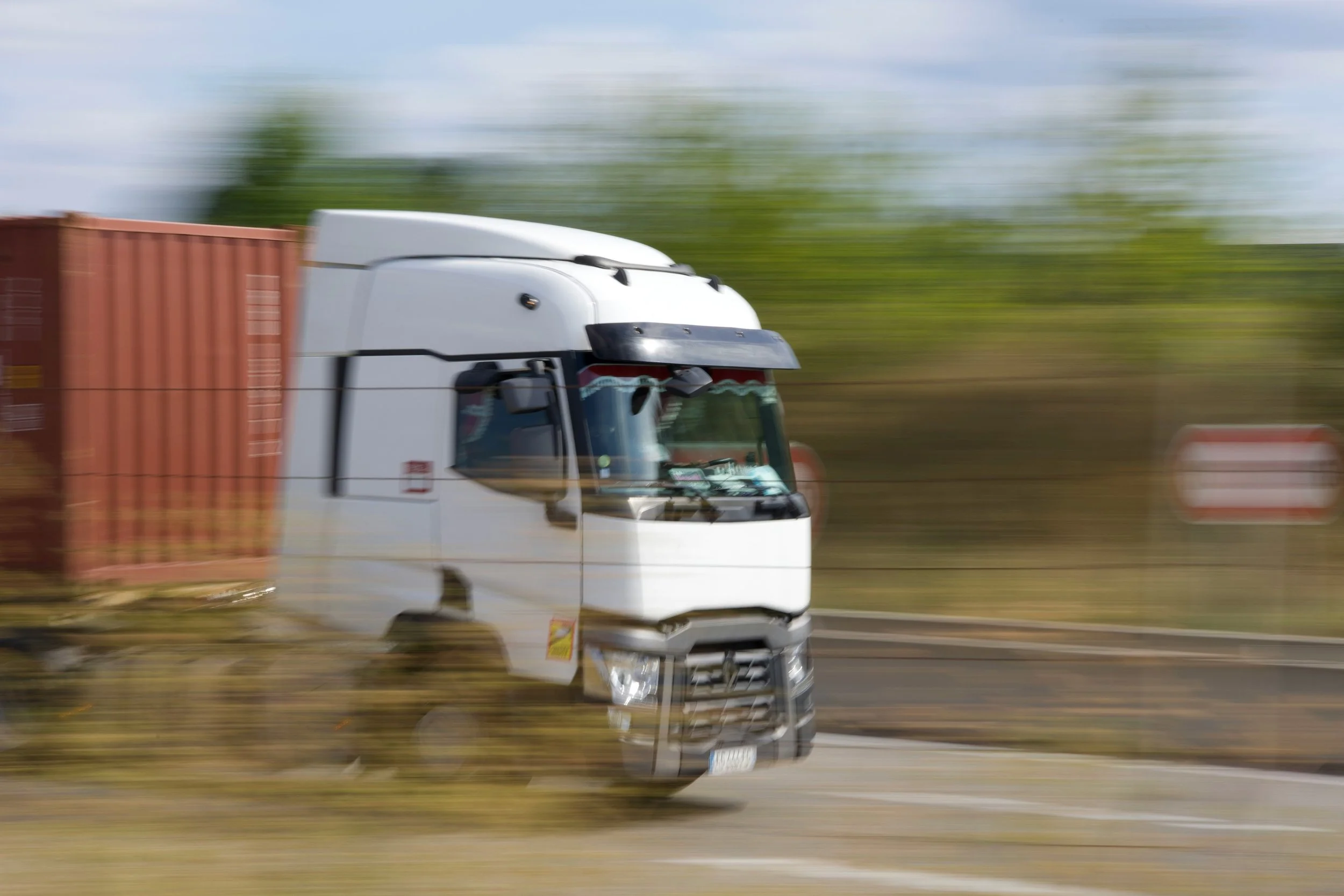Fast-moving white semi-truck with a red container on a highway, with background motion blur.