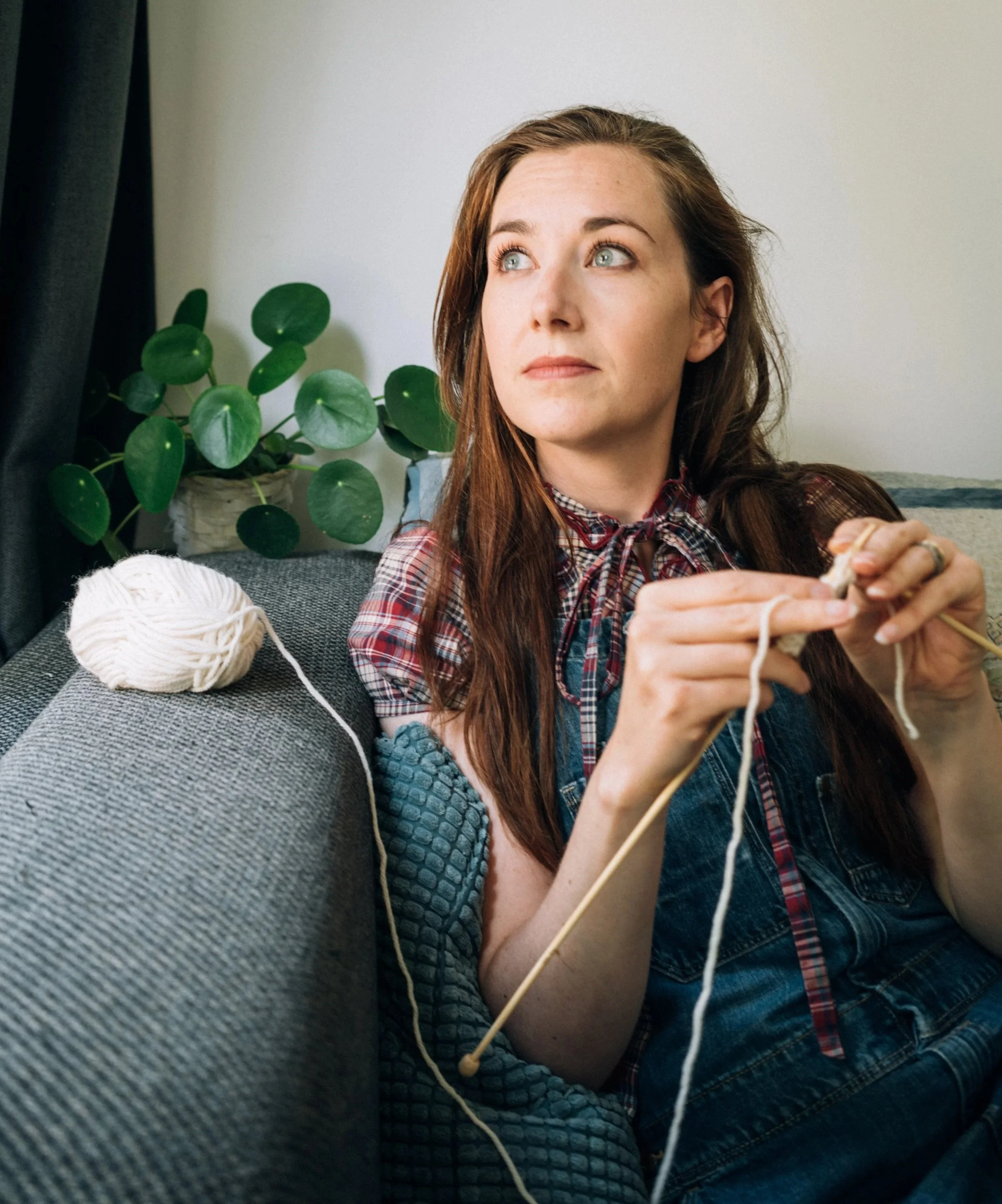 Knitting Teacher Alice sits knitting with cream yarn on a grey sofa