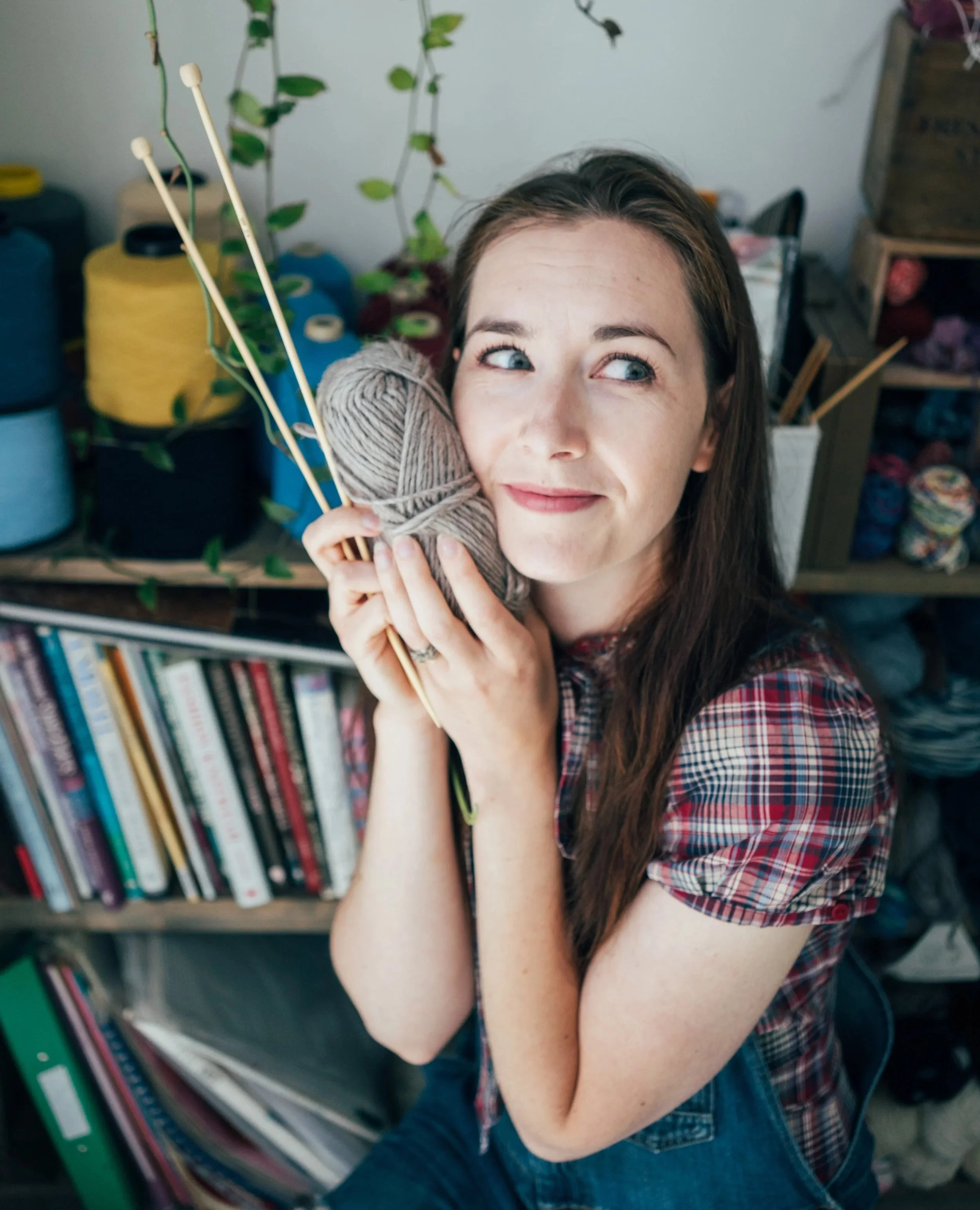 Knitting Teacher Alice holds beige yarn and wooden needles close to her left cheek