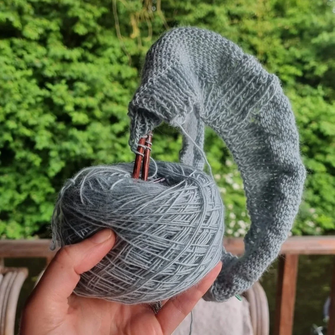 Blue Yarn with knitting attached is held up outside by a white hand