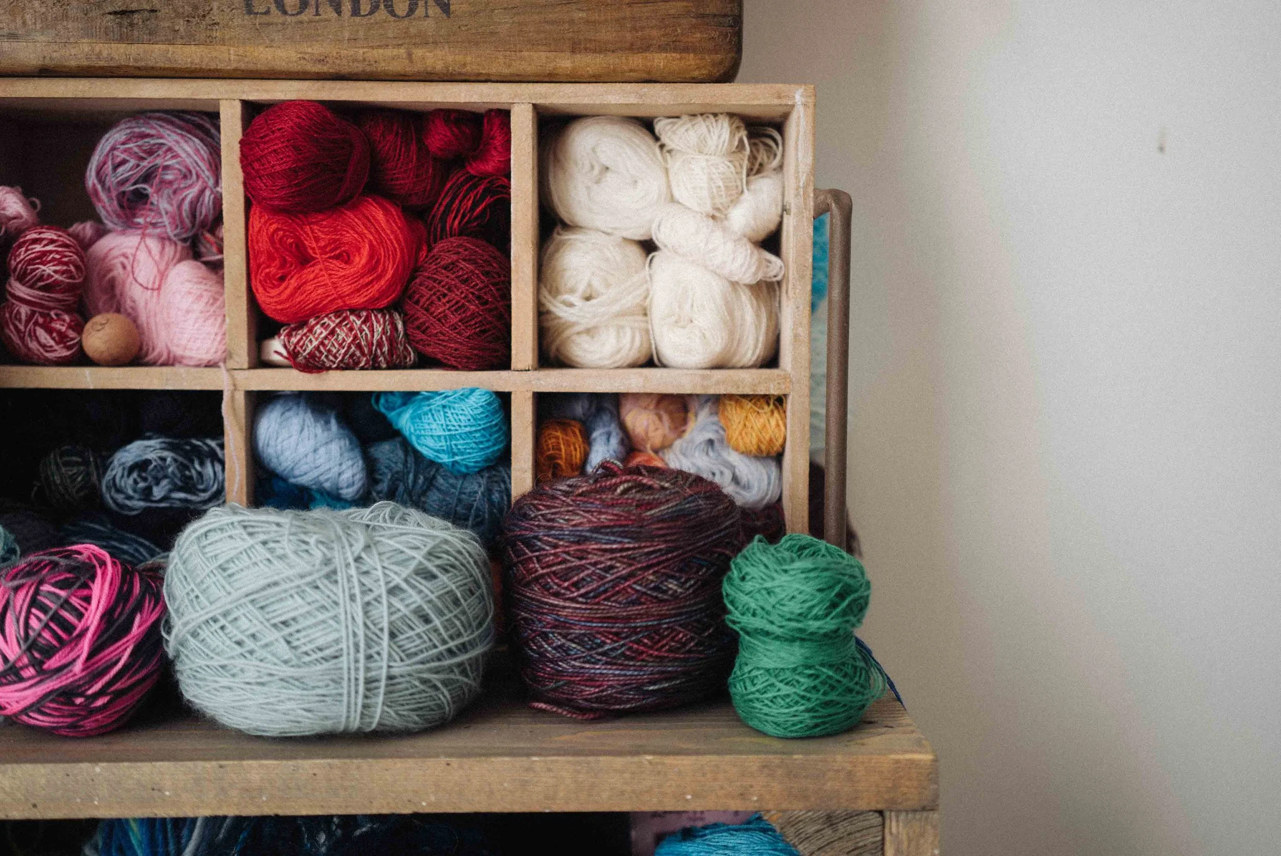 Close-up of a wooden yarn storage unit with multiple compartments filled with colorful balls of yarn.