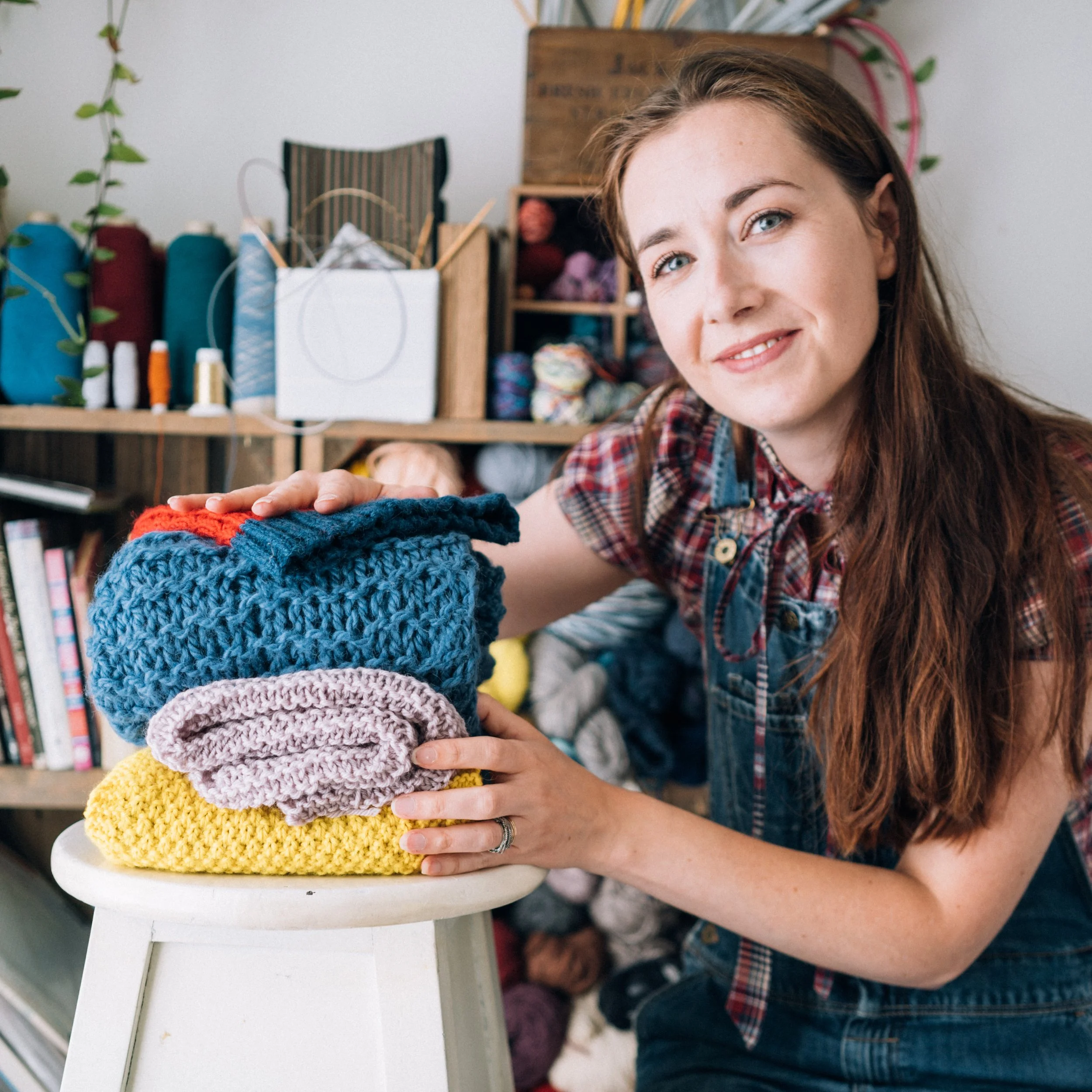 Knitting Teacher Alice has her hand on a pile of handknitted items