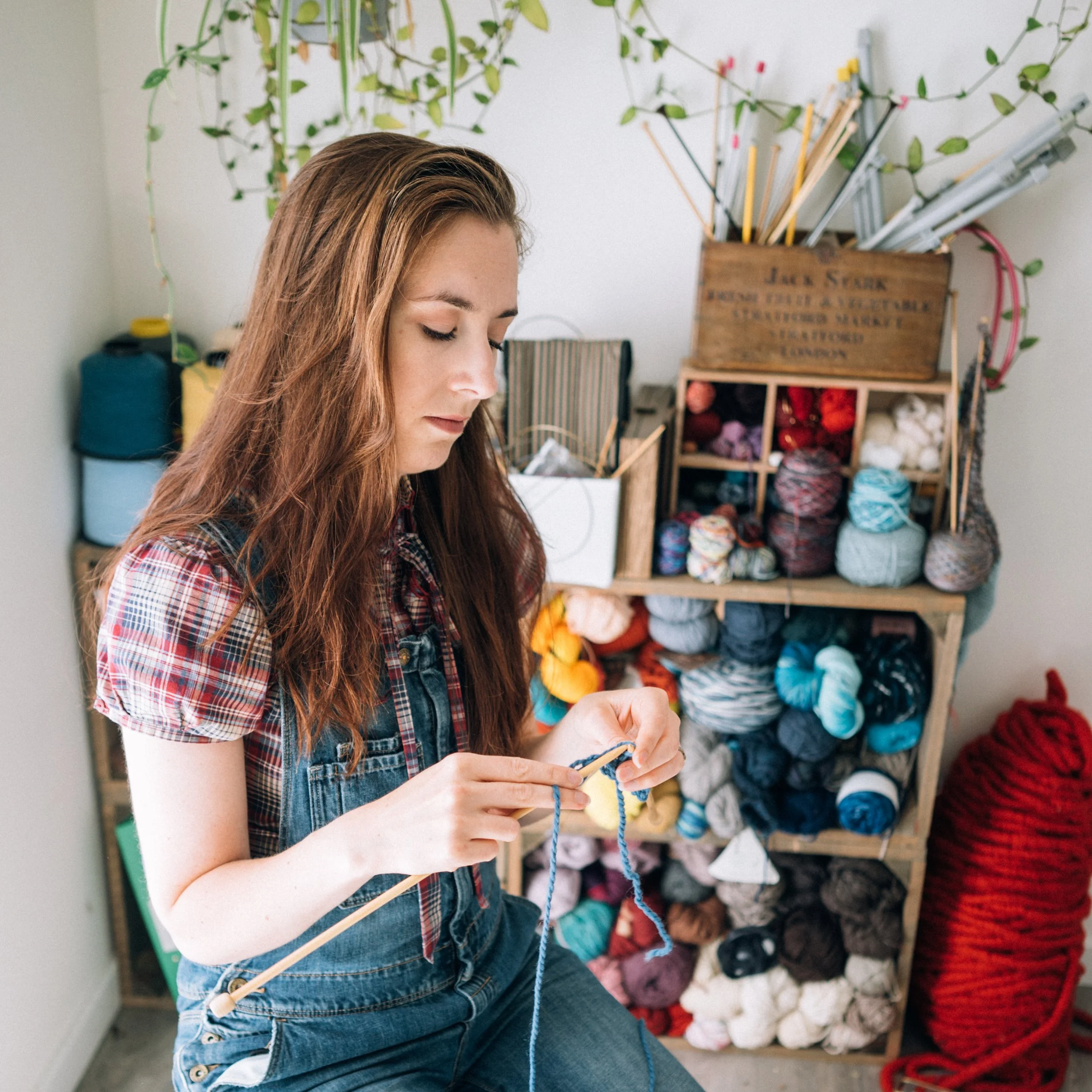 Knitting Teacher Alice knitting in her studio with yarn and knitting needlesbehind her