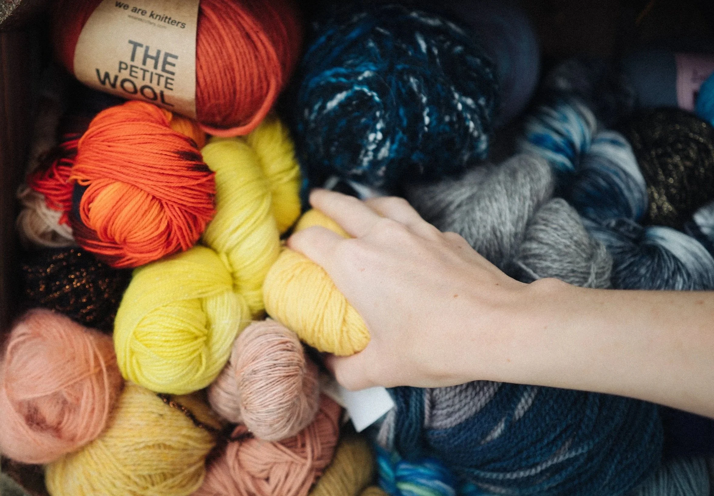 A white female hand reaches into a bundle of different coloured knitting yarn
