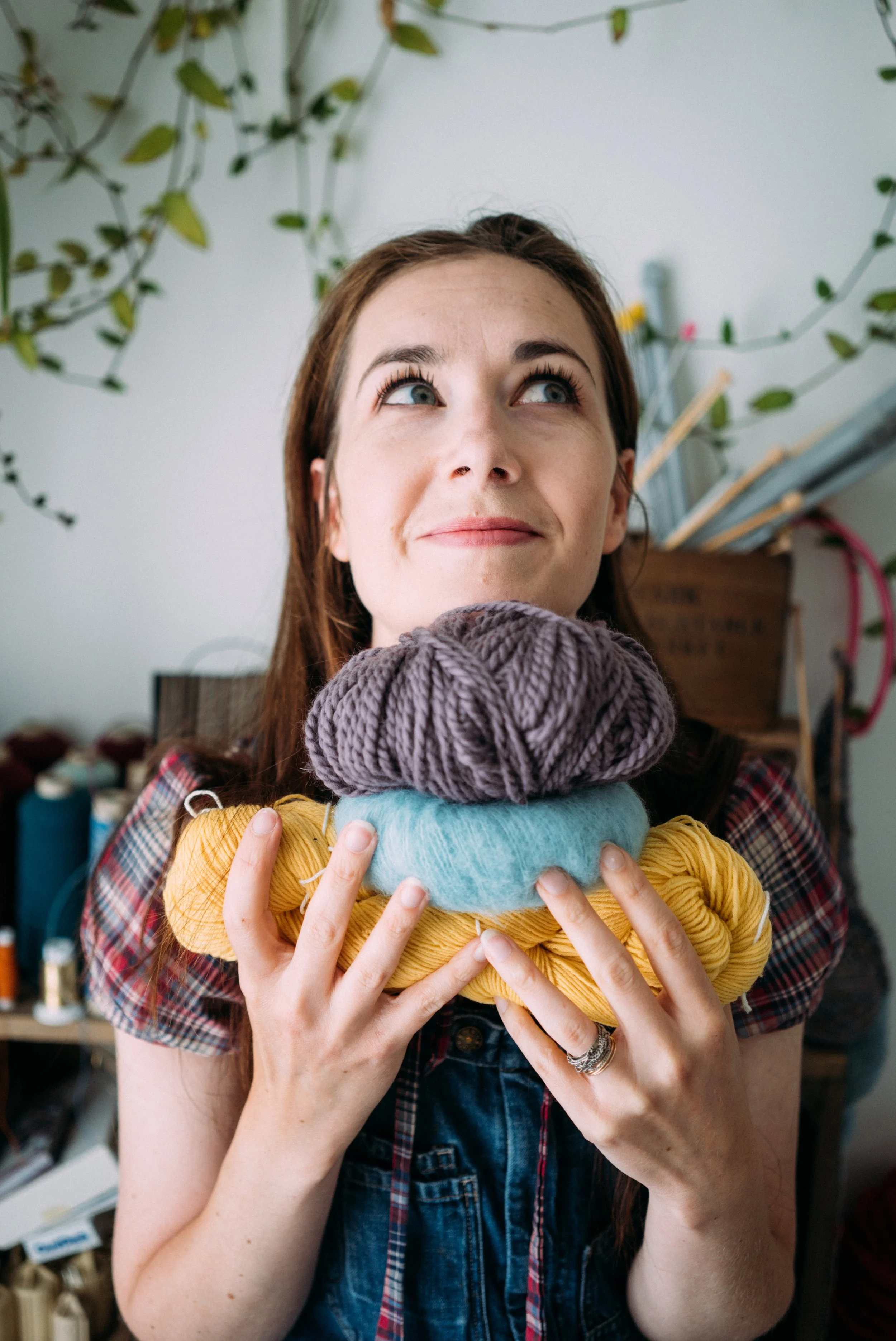 Alice, a knitting teacher holds a stack of knitting yarn looking up to the top right