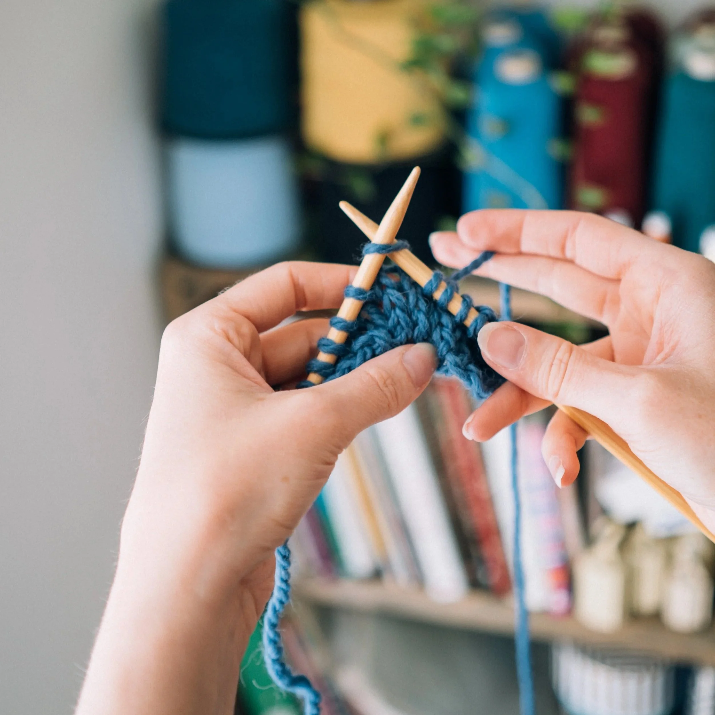 Blue yarn on wooden knitting needles, held out by a knitting teacher's hands