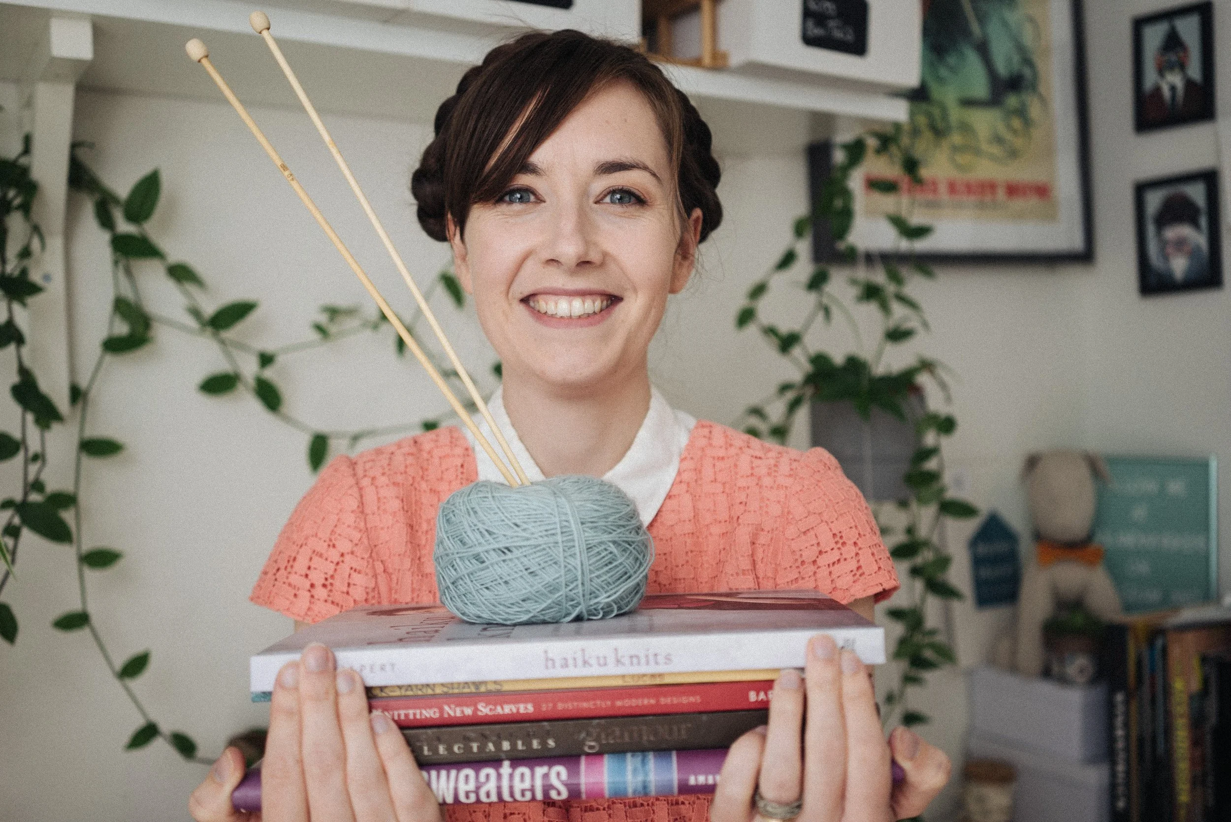 Knitting Teacher Alice holds knitting books with blue yarn and wooden needles on and smiles