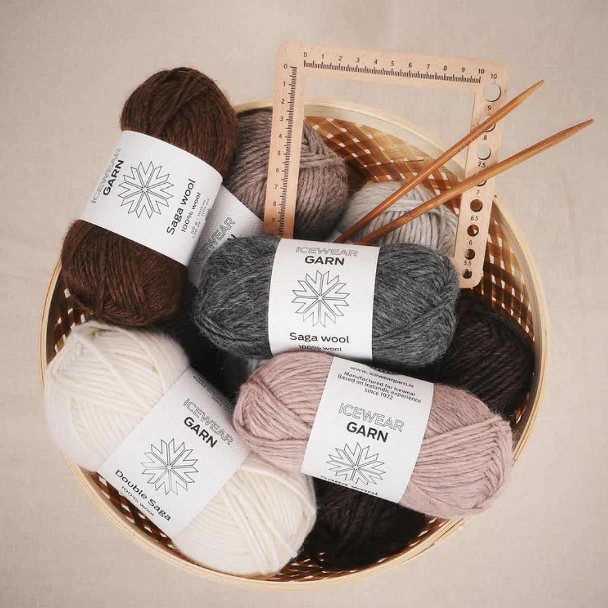 A basket of pink, cream, grey and brown Icewear yarn sits with knitting needles and notions