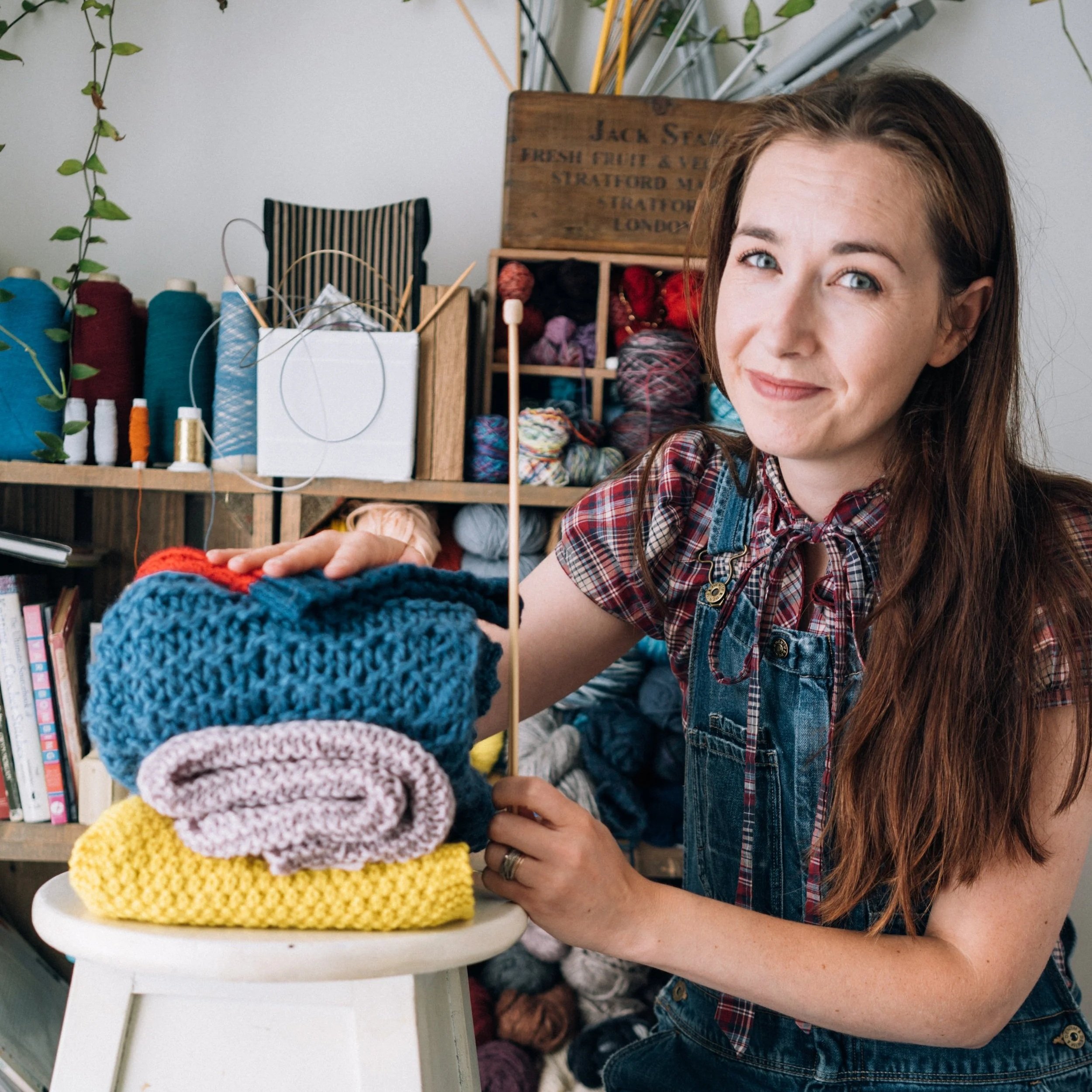 Knitting Teacher Alice kneels beside a pile of handknit pieces looking proud