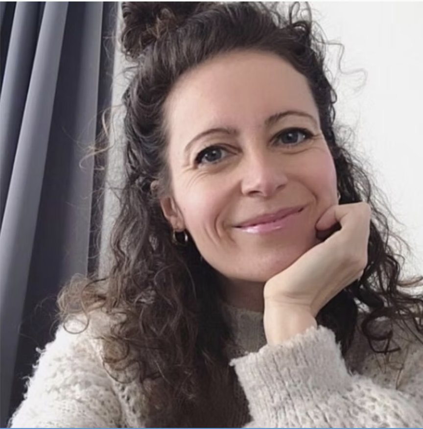 Claudia, a white woman with dark curl hair smiles at the camera