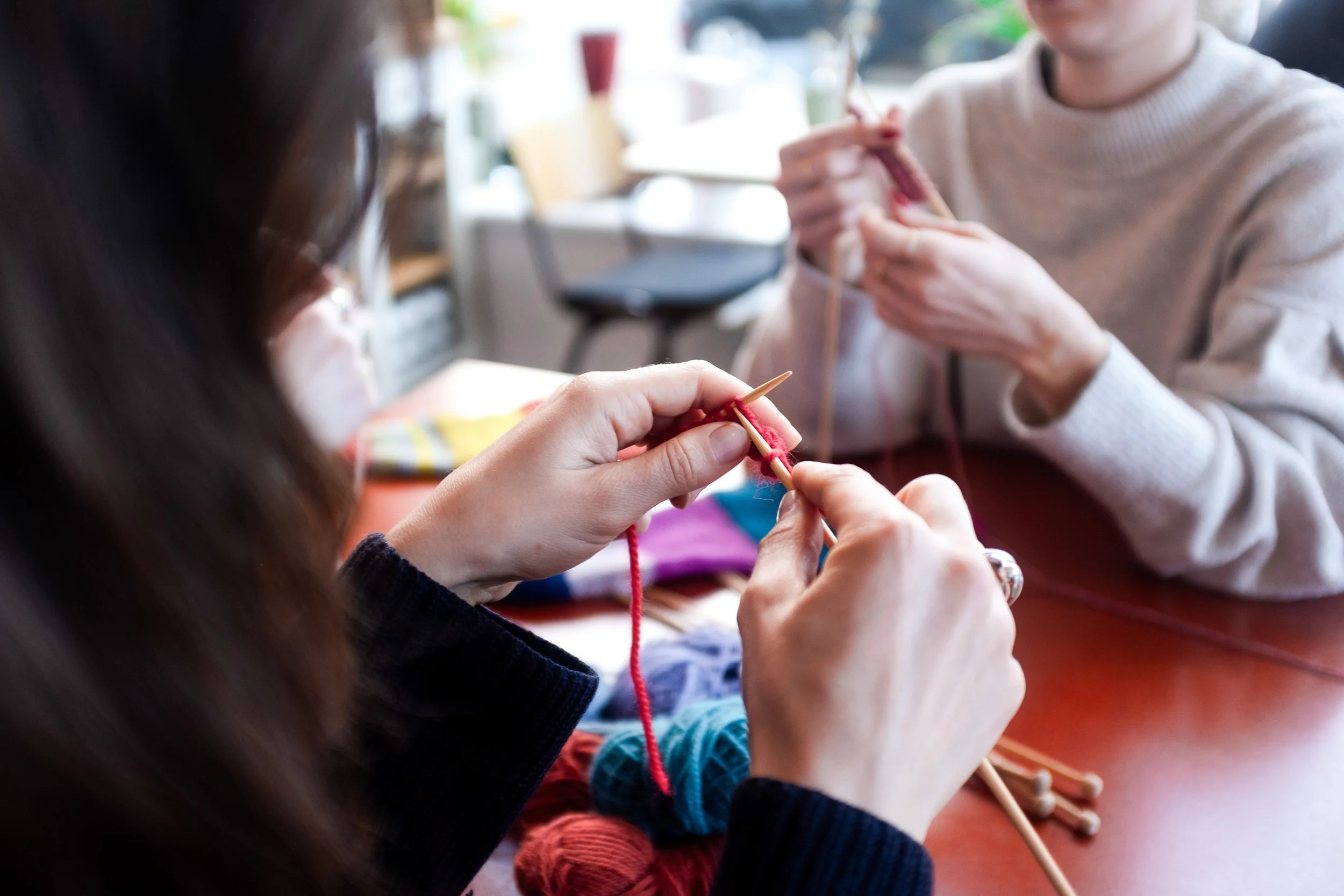 White female beginner knitter knits with red yarn and wooden needles