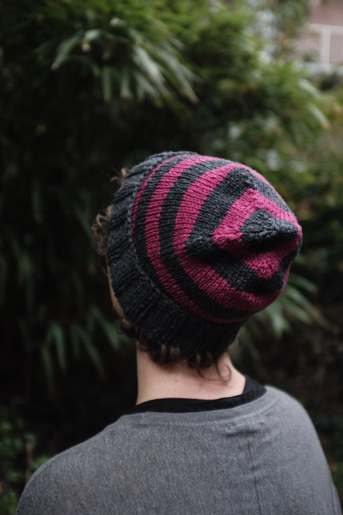 A white female wears a pink and grey striped hand knitted beanie hat outside