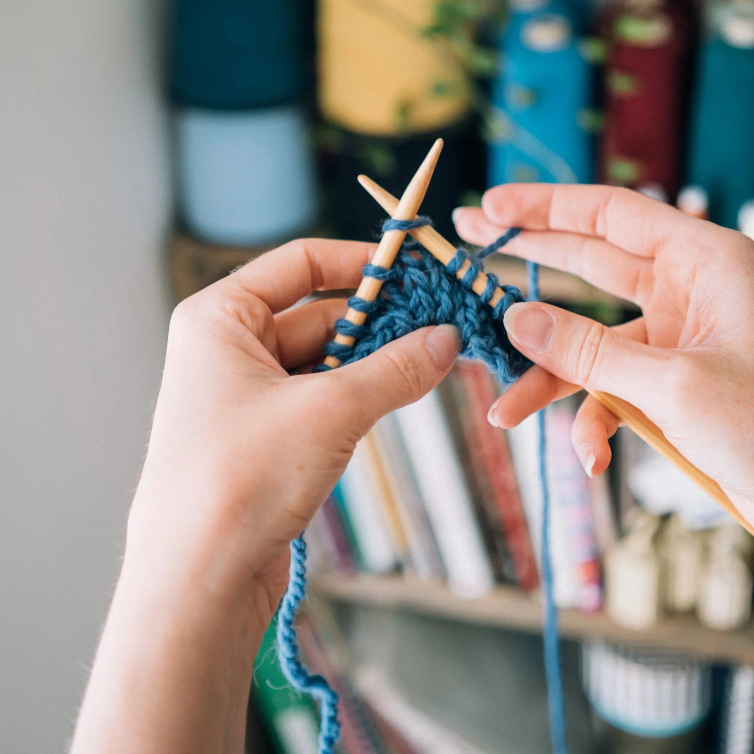 white female hands hold blue yarn knitting on wooden needles