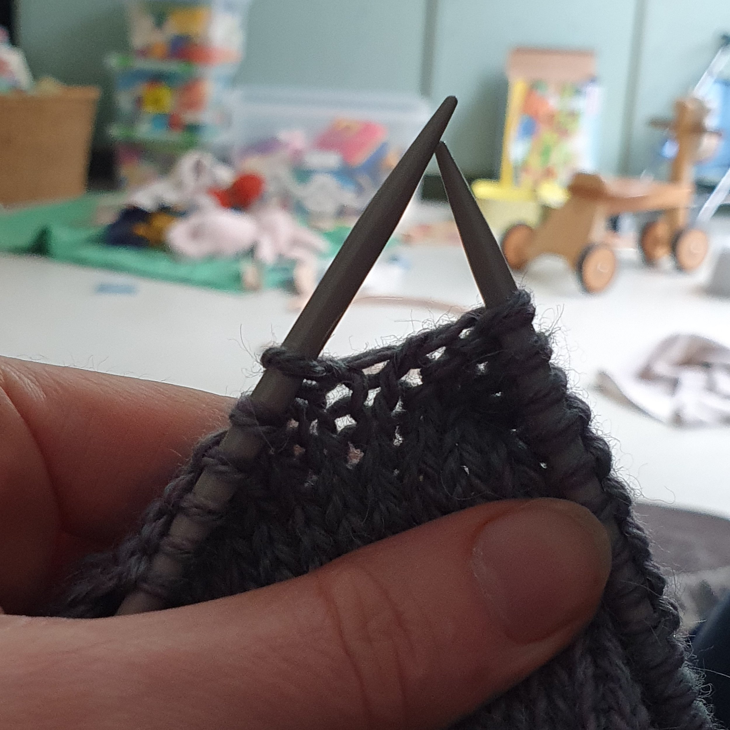 Knitting on Needles with a background visible of baby toys