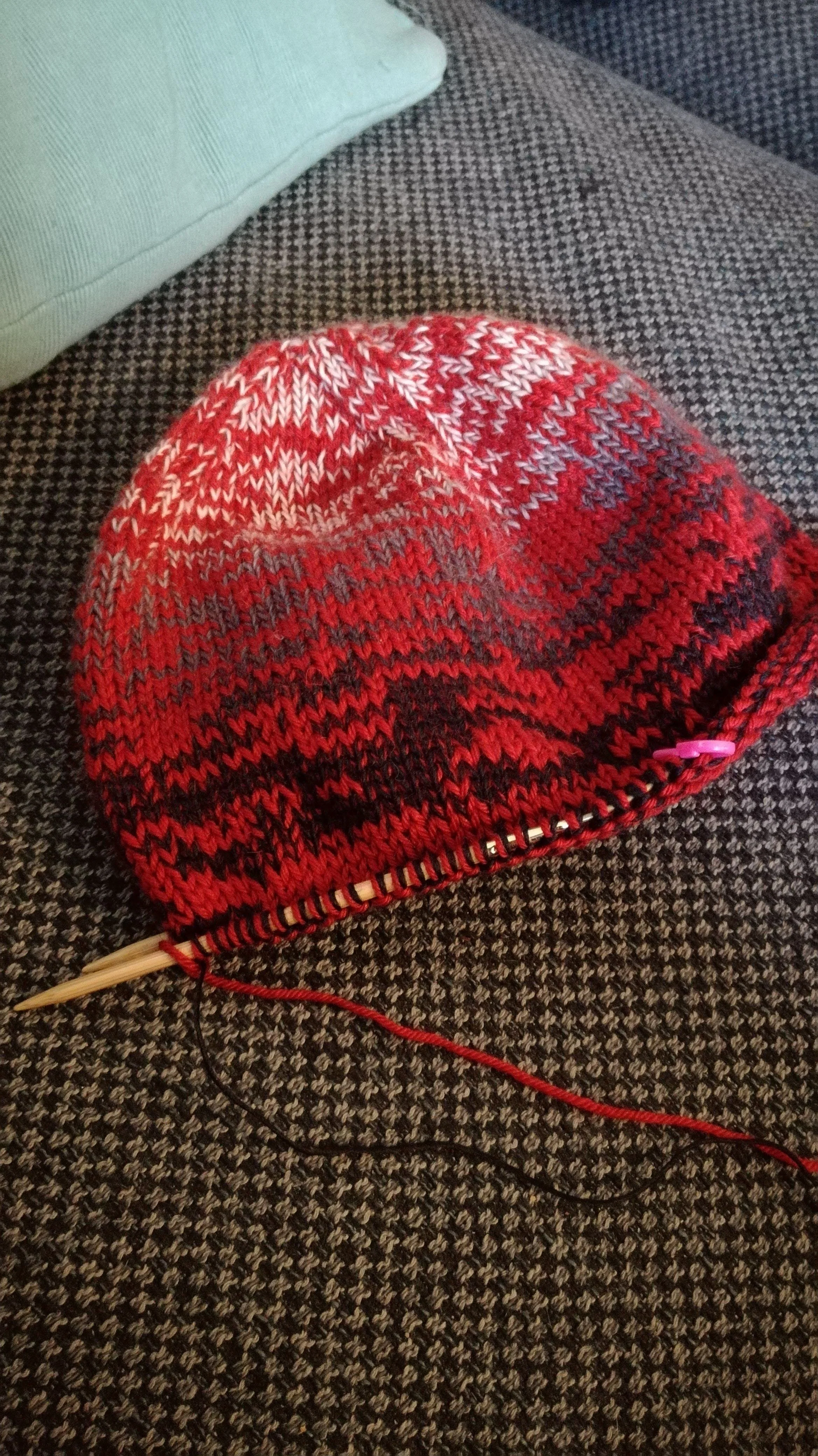 Half a knitted red and black hat lies on a sofa