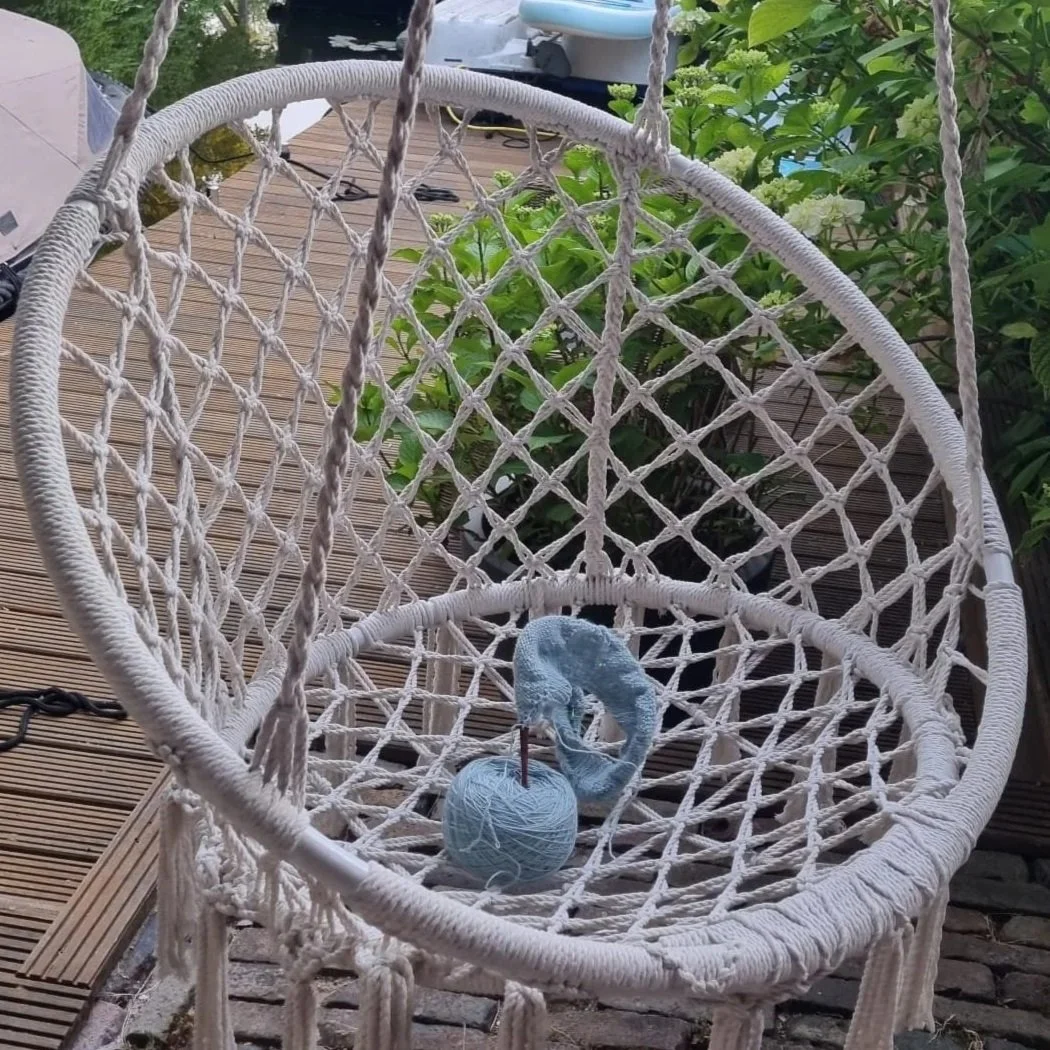 Blue Yarn and needles sit on a swinging garden chair beside greenery and water