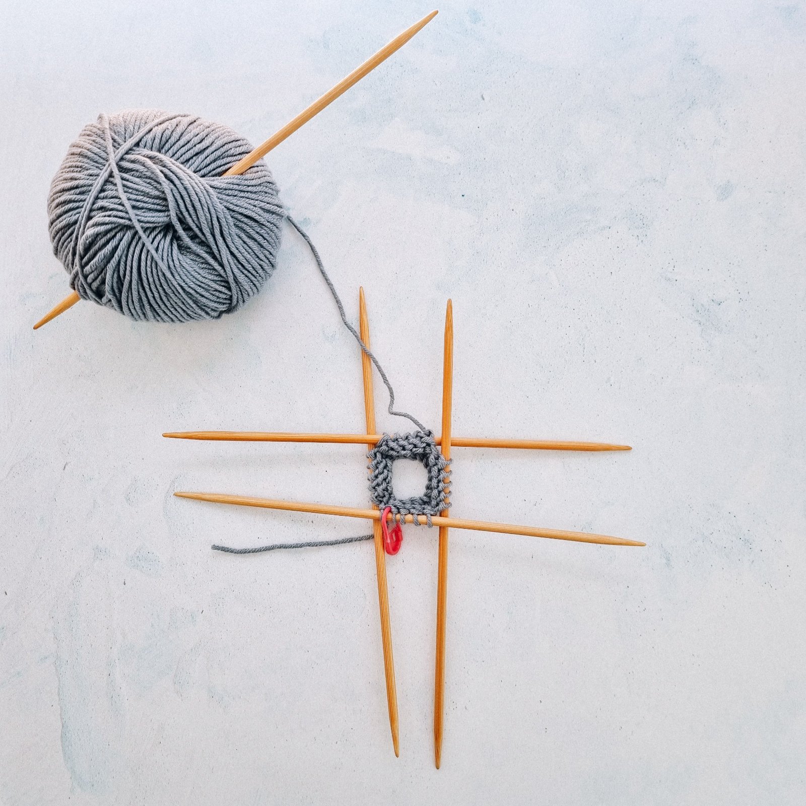 Double Pointed wooden needles with blue yarn and knitting demonstrating how to knit in the round