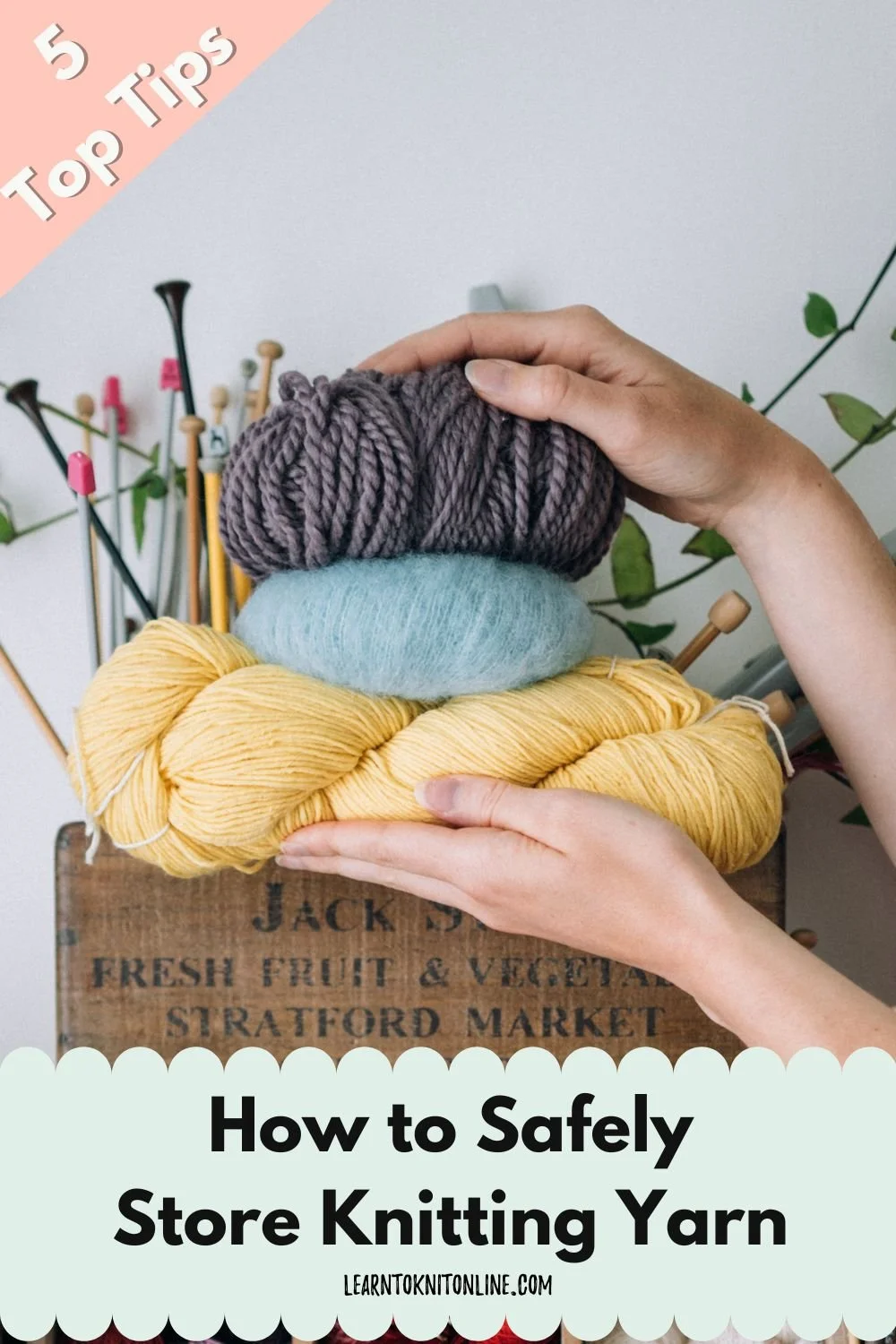 White female hands hold a stack of yarn balls with knitting needles in the background