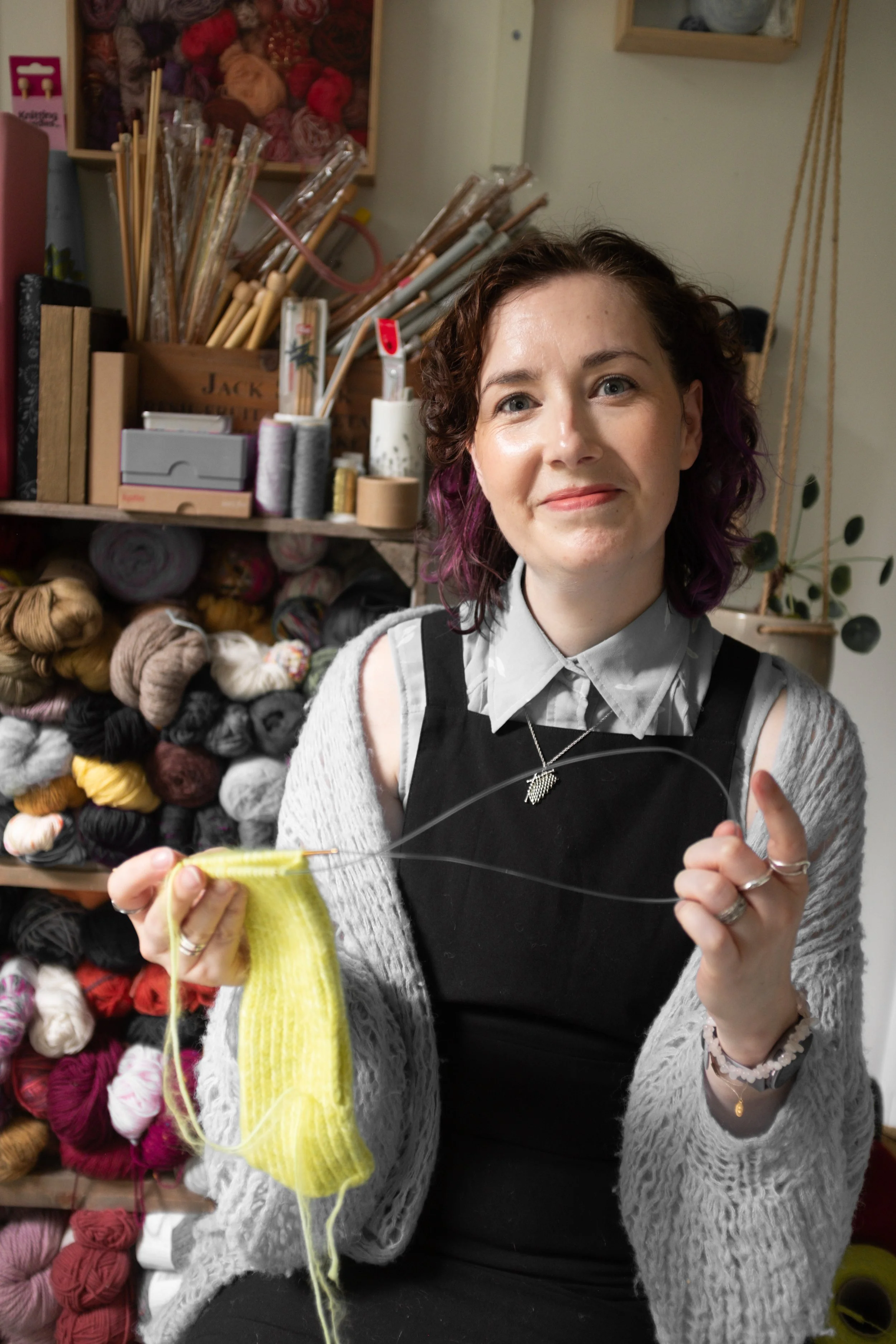 Alice, a knitting teacher holds yellow knitting and smiles at the viewer