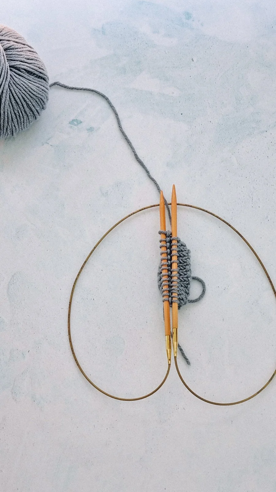 Knitting in progress on circular needles with gray yarn and a ball of gray yarn nearby.