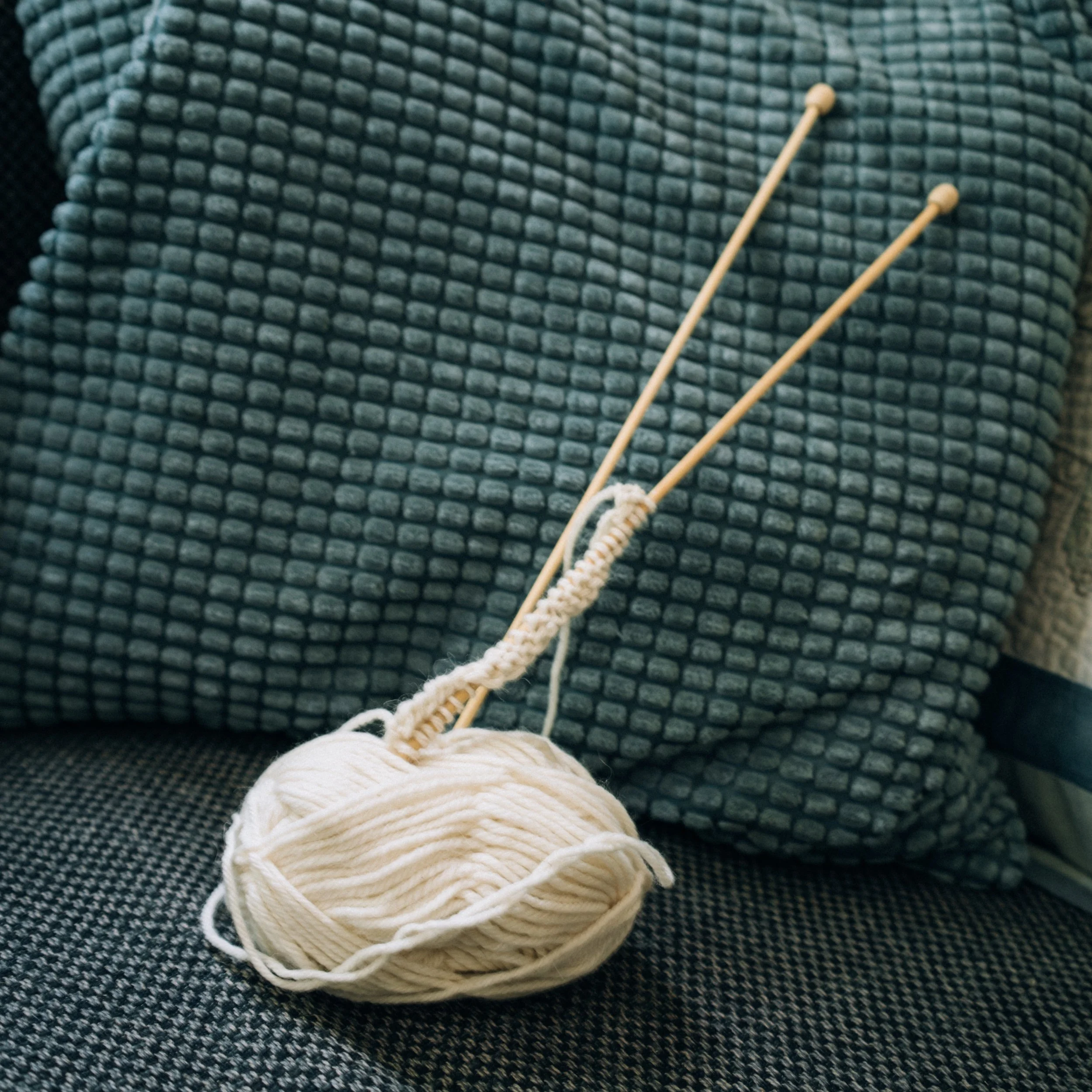 Cream Yarn with Knitting Needles sits on a sofa