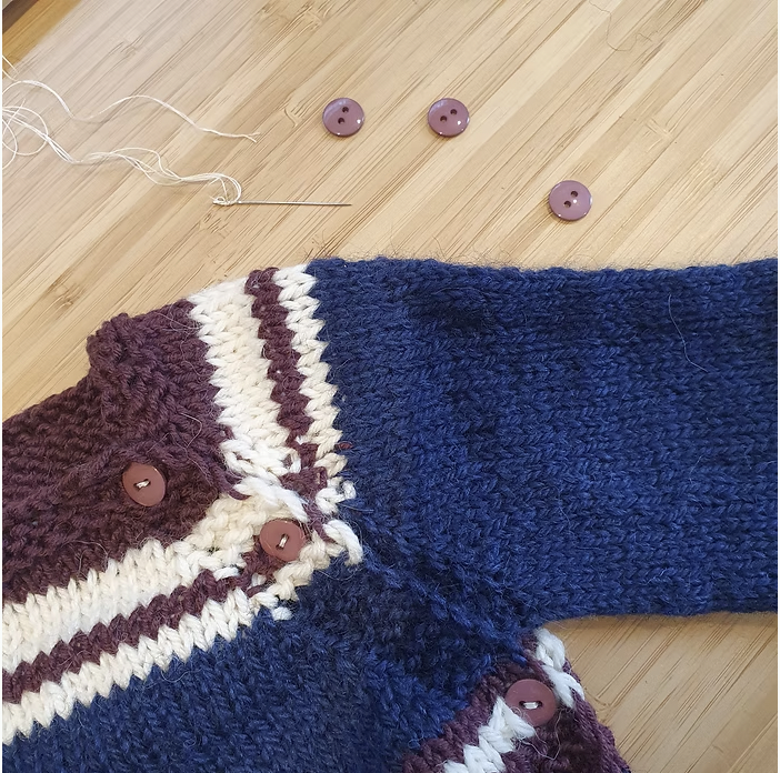 A partial view of a baby cardigan in view with buttons, needle and thread