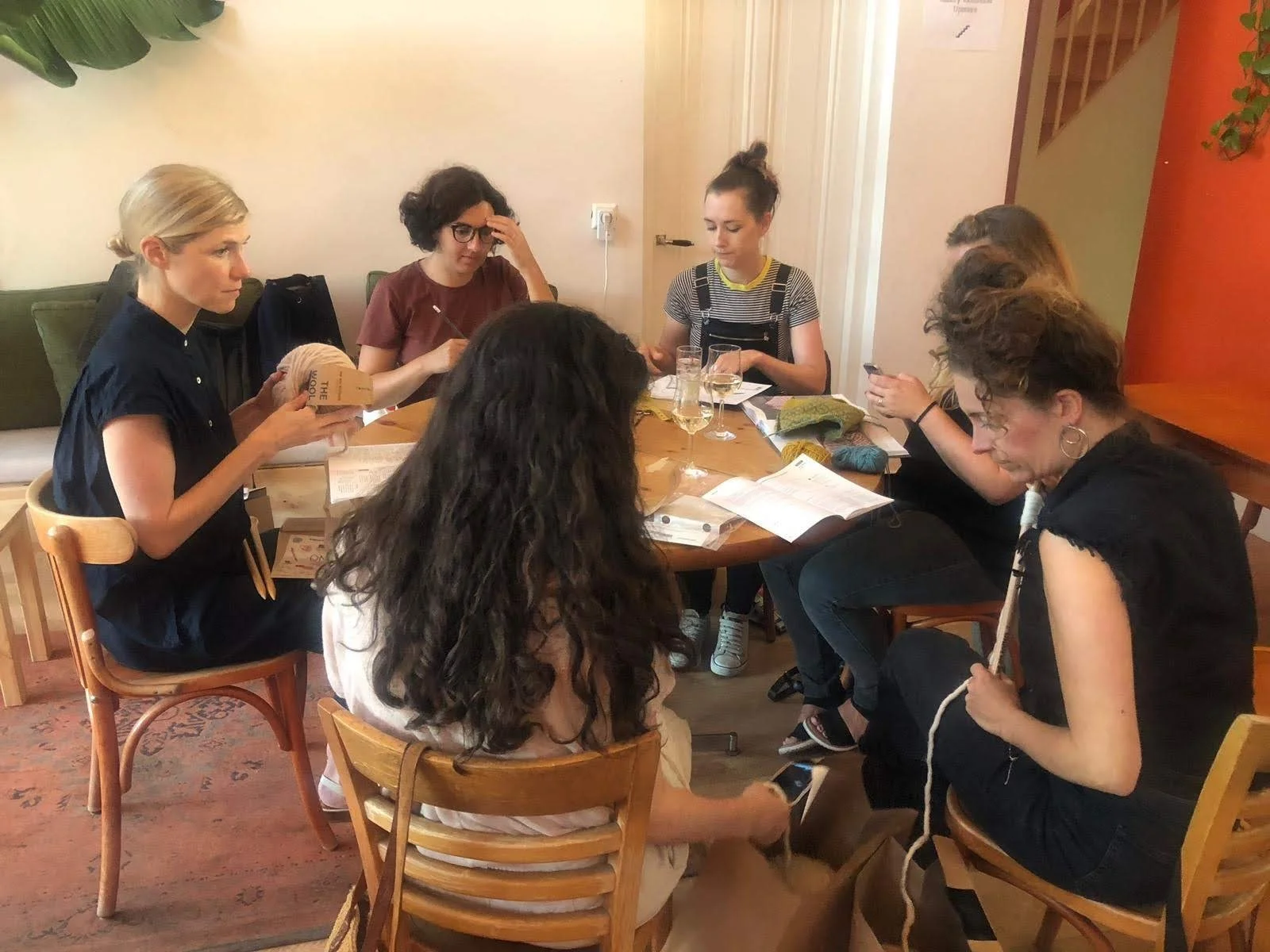 A group of woman sit around a round table together knitting
