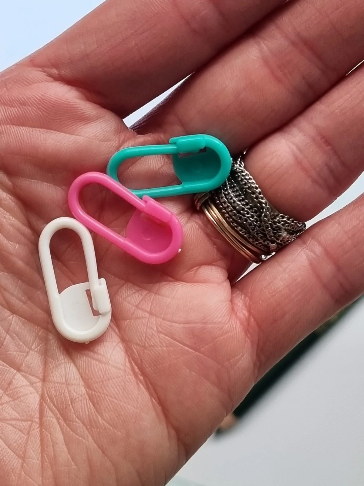 A white female hand holds 3 differently coloured plastic stitch markers