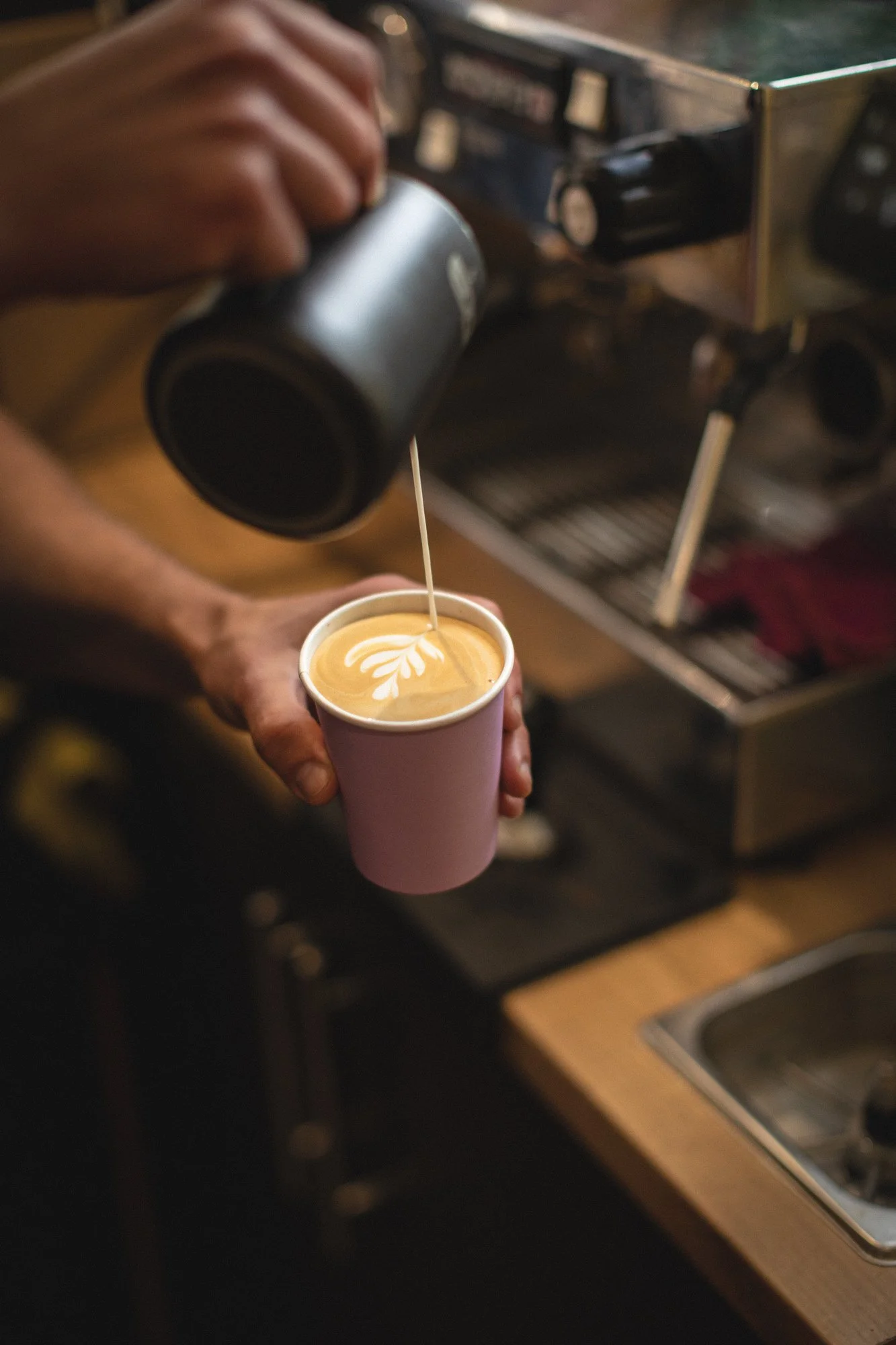 Barista pouring steamed milk into a cup of espresso to create latte art.