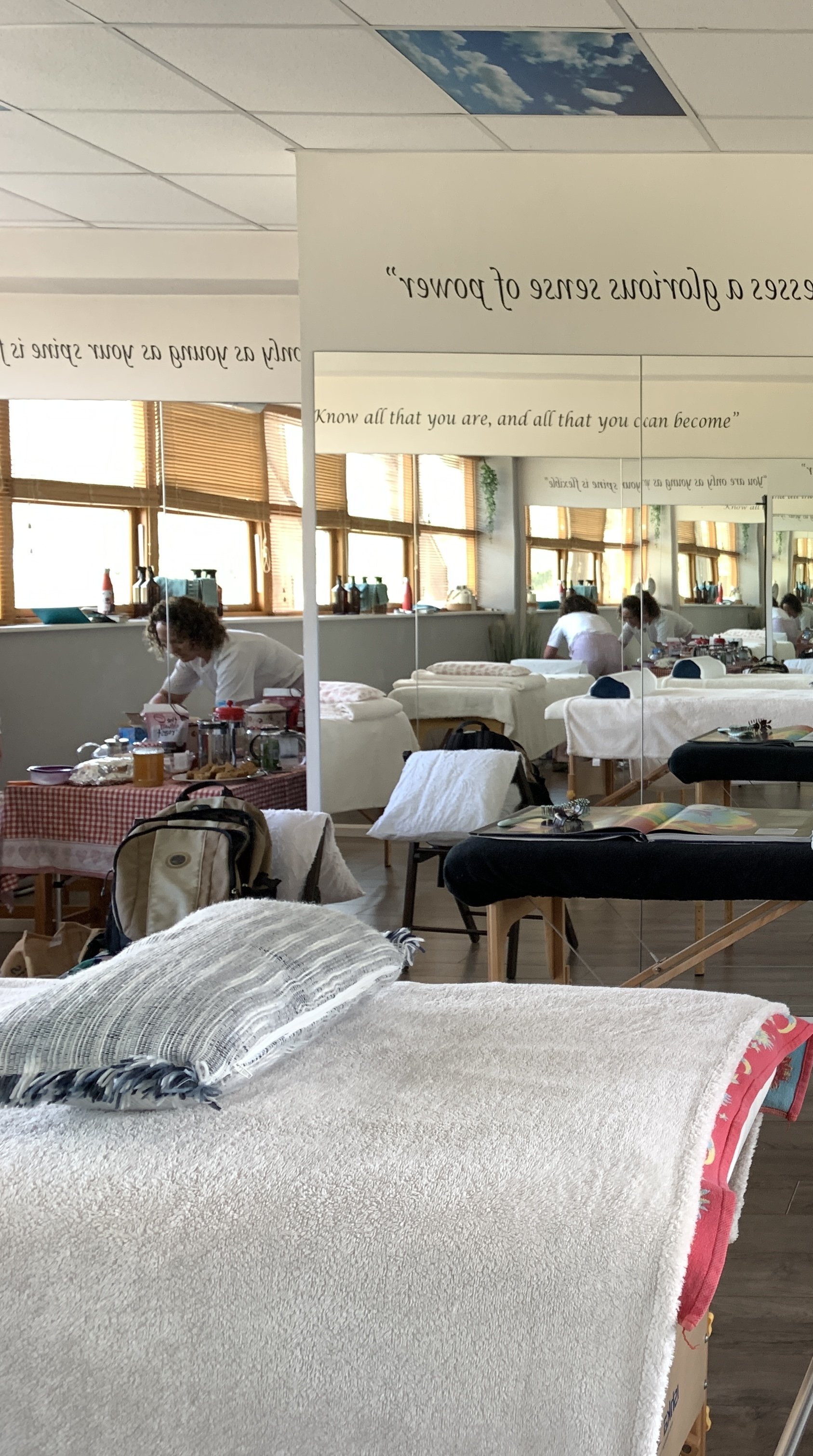 Massage therapy room with beds, towels, and supplies, reflected in a mirror with a quote about self-love.