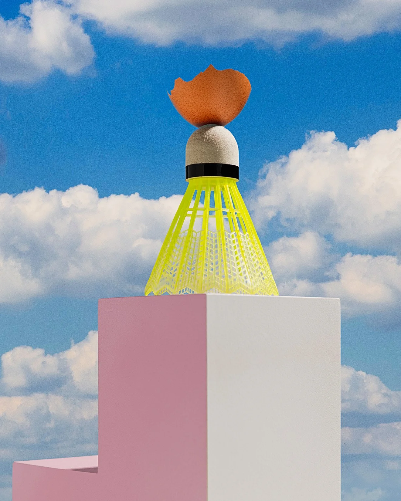 A surreal sculpture of a cracked eggshell with a yolk on top, supported by a yellow conical structure, placed on a pink and white platform against a background of blue sky and clouds.