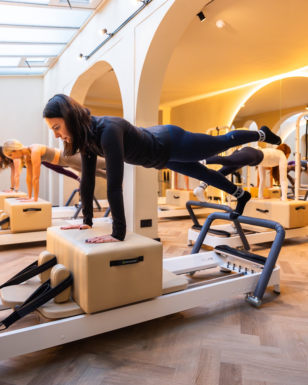 Women exercising on Pilates reformers during a fitness class in a well-lit studio.