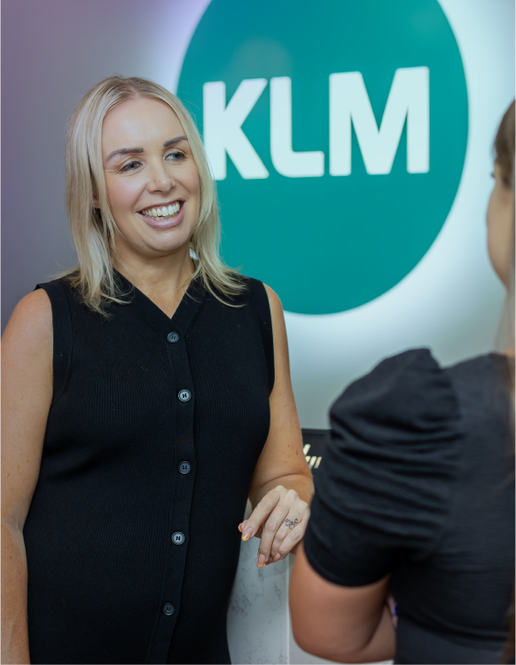 Two women talking in front of a KLM logo at an office