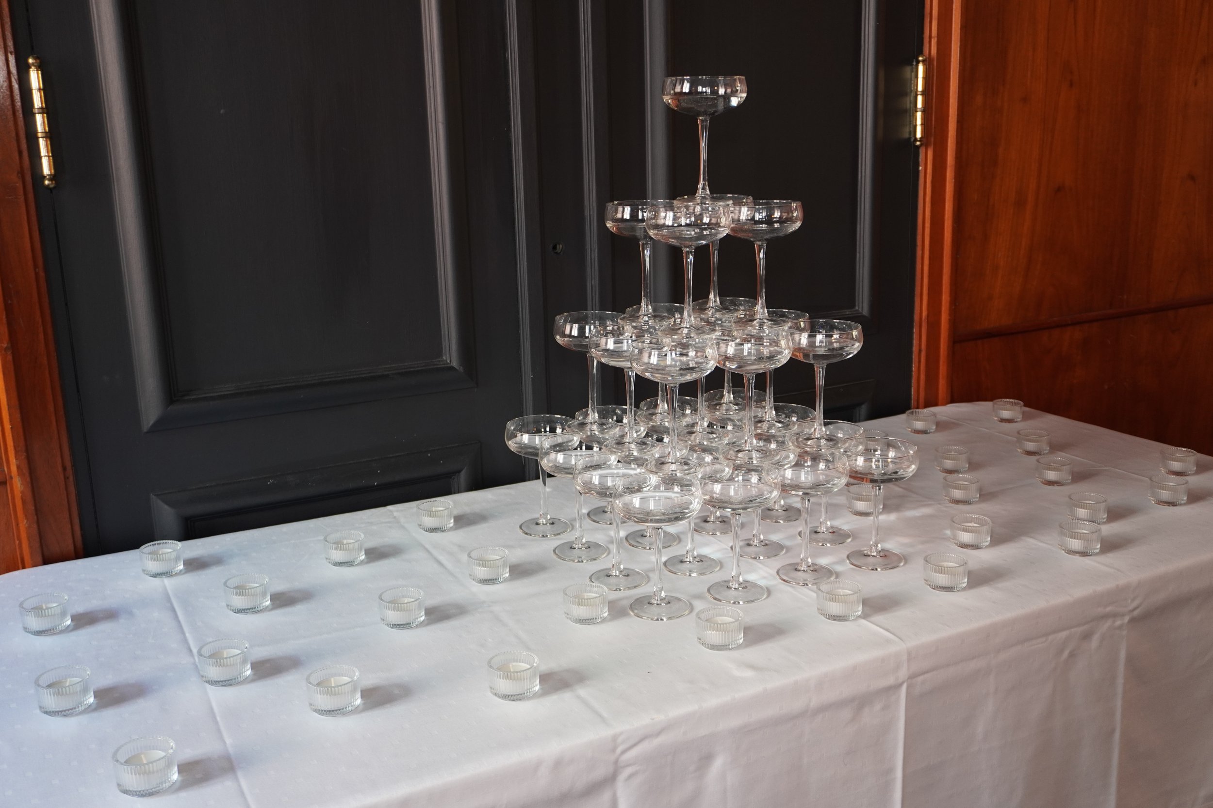 Elegant middagsbord dekket med hvit duk, tomme hvite tallerkener, glass, og svarte servietter i vinglass, med en liten blomsteroppsats i midten.