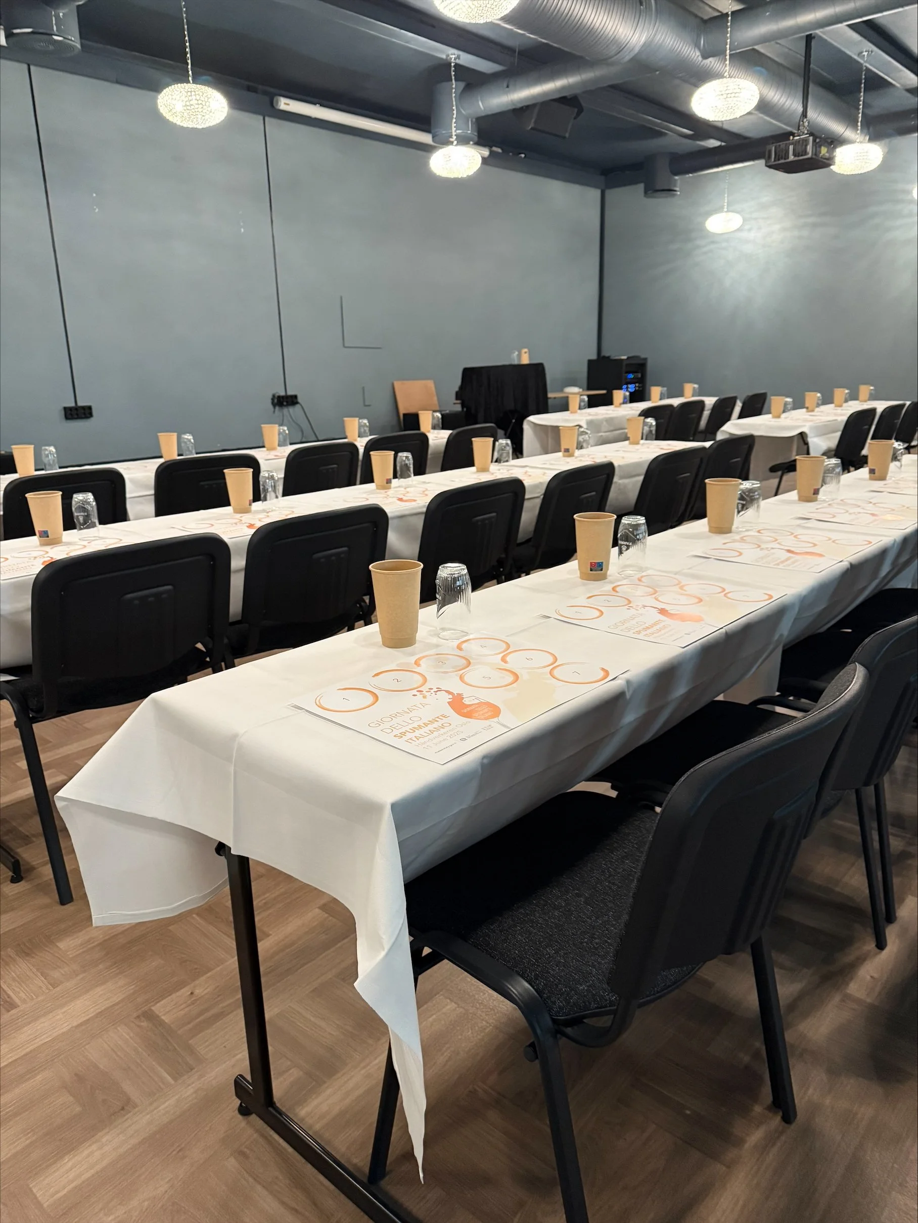 Et konferanserom satt opp med langbord dekket med hvite duker, plastkopper og vannglass, klare for en gruppearrangement.