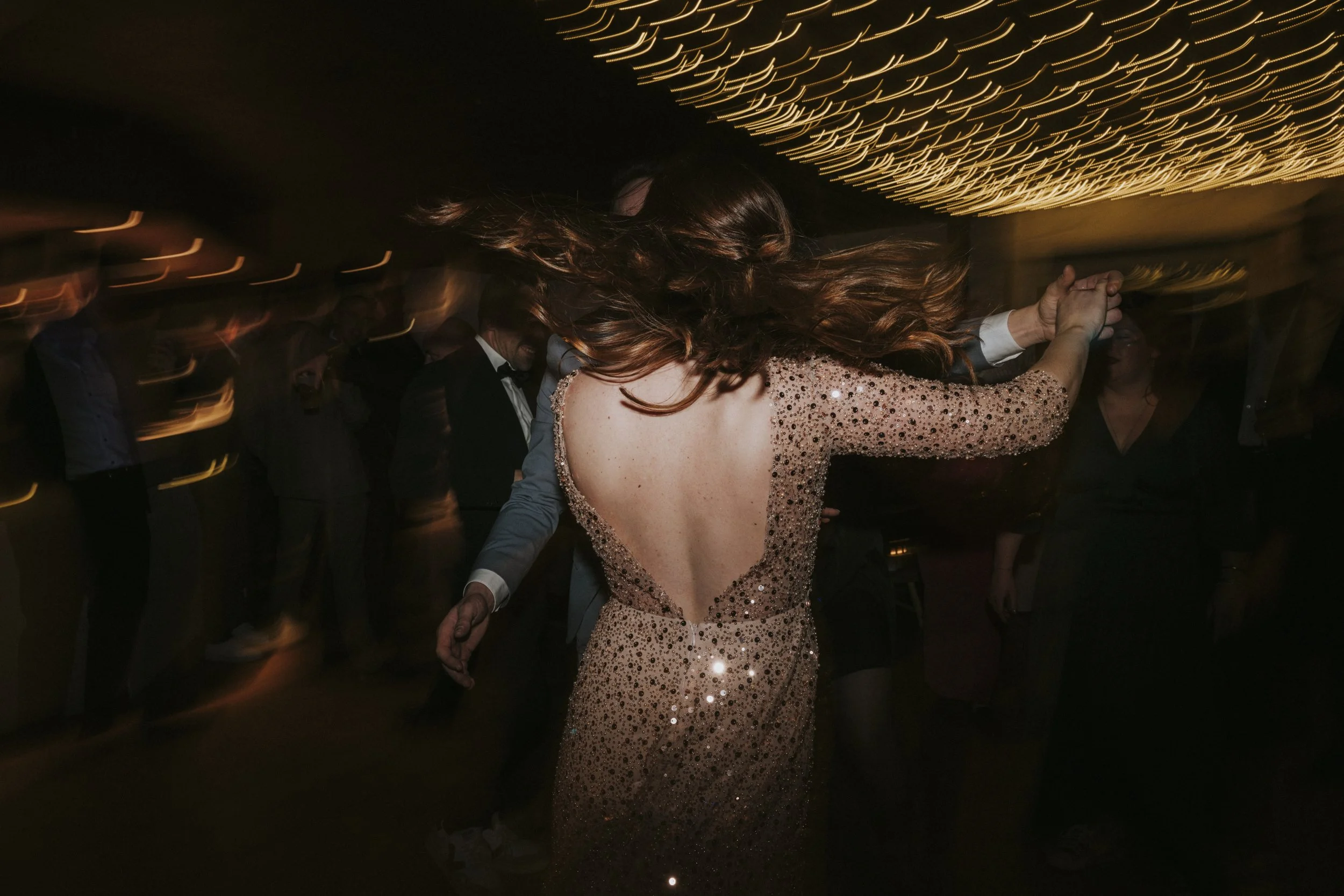 Une femme avec une robe longue à sequins roses, tournant lors d'une fête ou d'une danse, avec des lumières en arrière-plan.