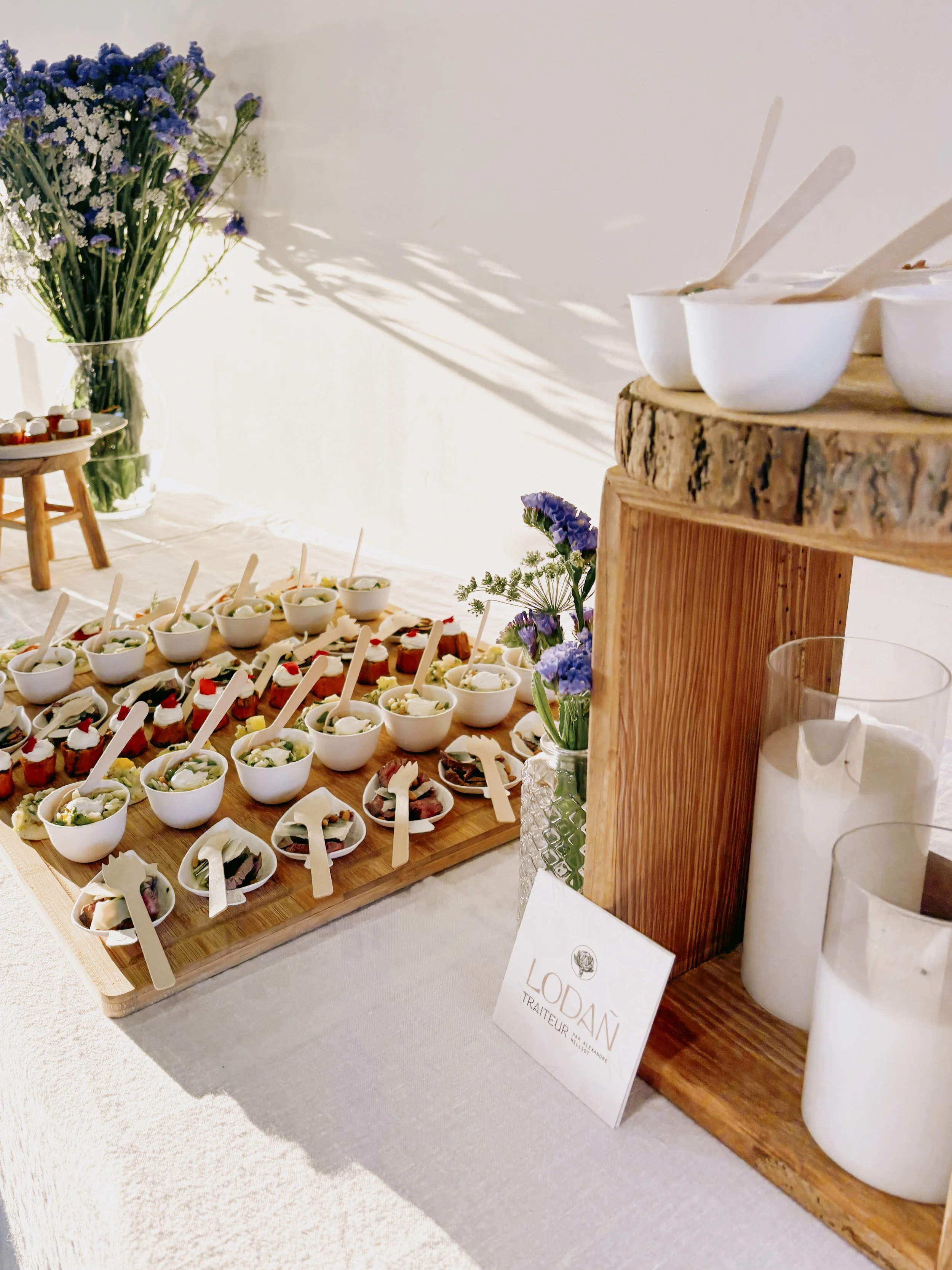 Plateau de dégustation avec petits bols de nourriture, fleurs violettes, et bougies, décoré dans un style naturel et élégant.