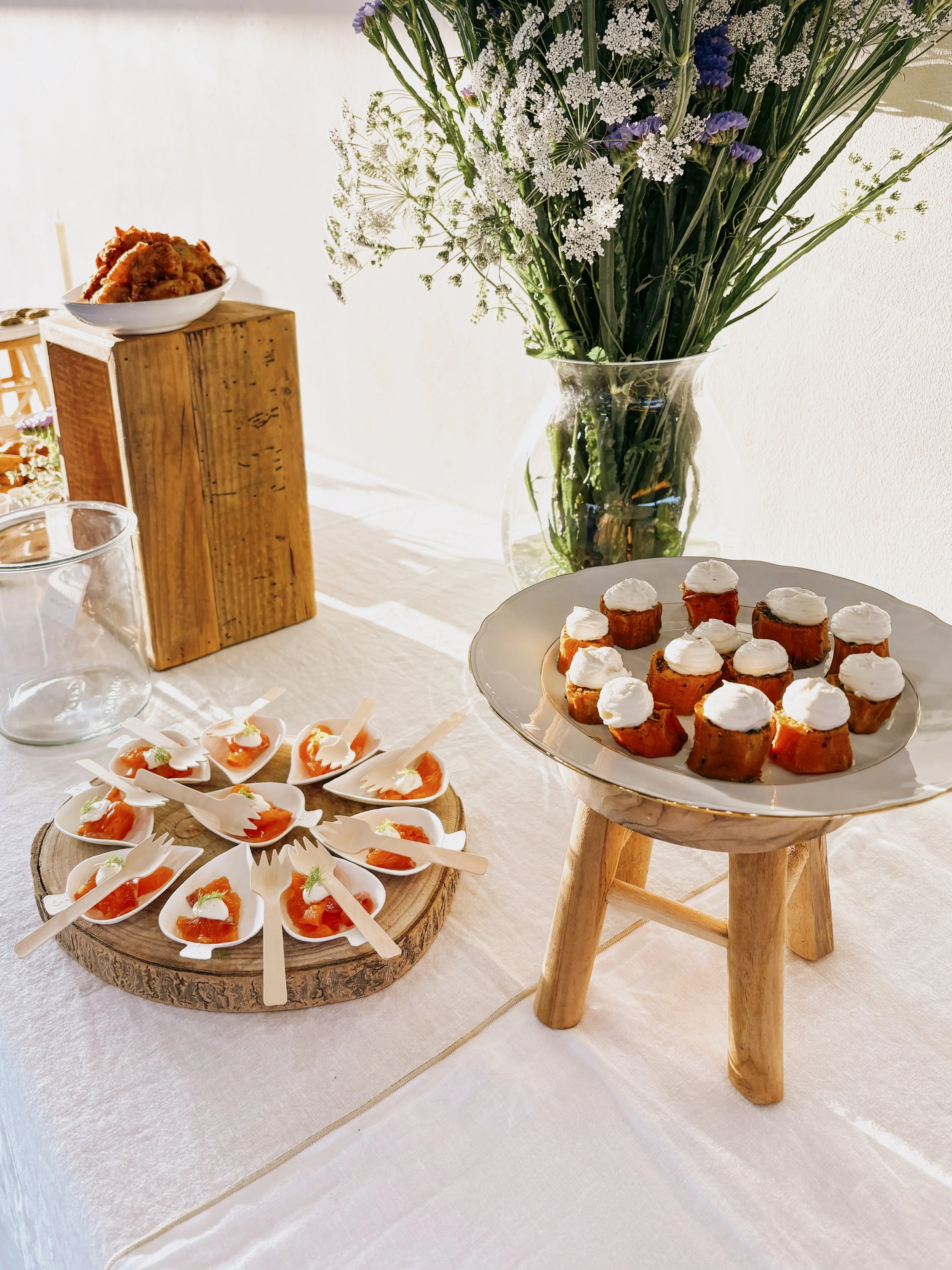 Plaque avec canapés et amuse-bouches à proximité d'un vase avec des fleurs, sur une table ou un buffet.