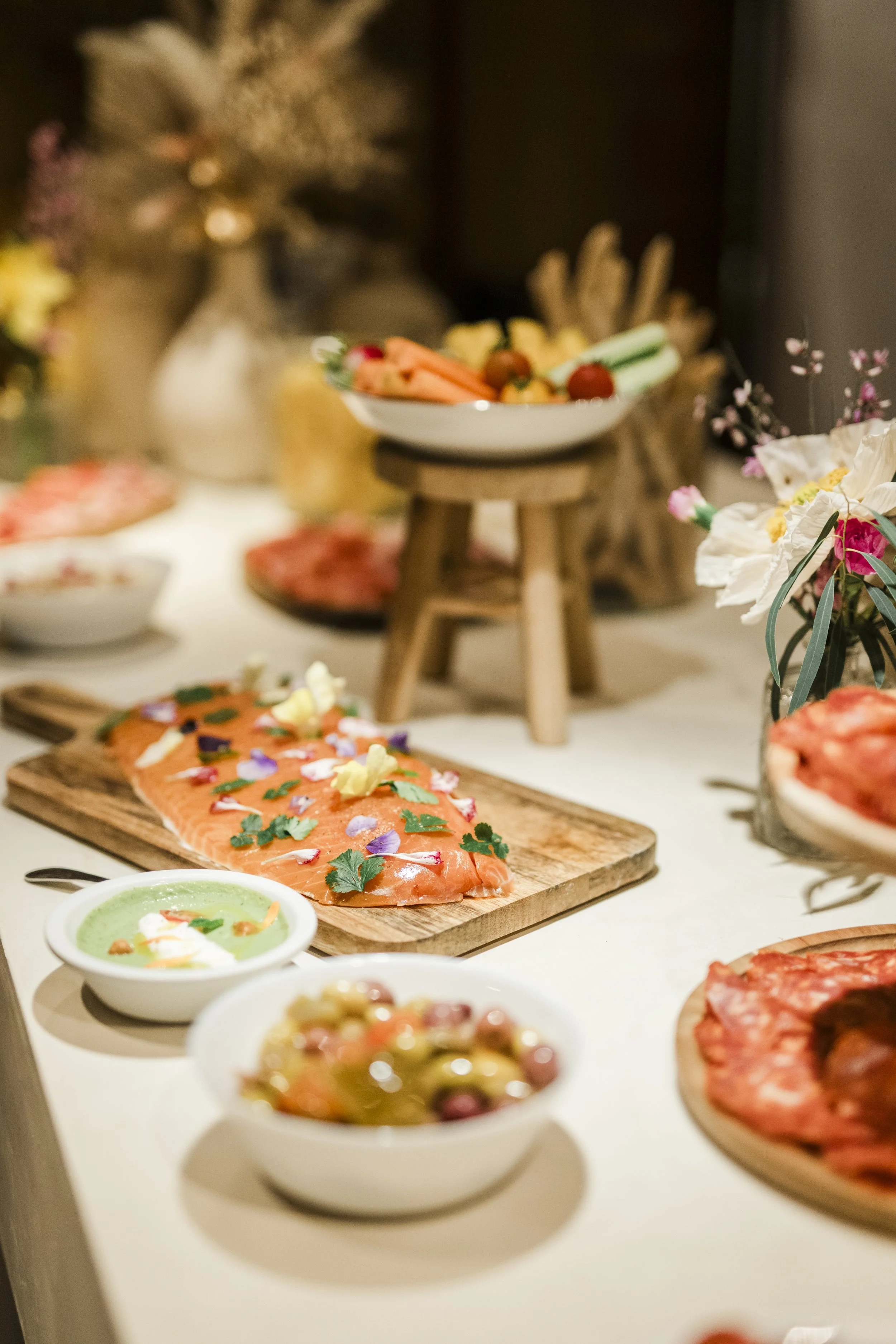 Plat de saumon cru orné de fleurs et de feuilles, accompagné de sauces et autres plats, sur une table avec des fleurs décoratives.