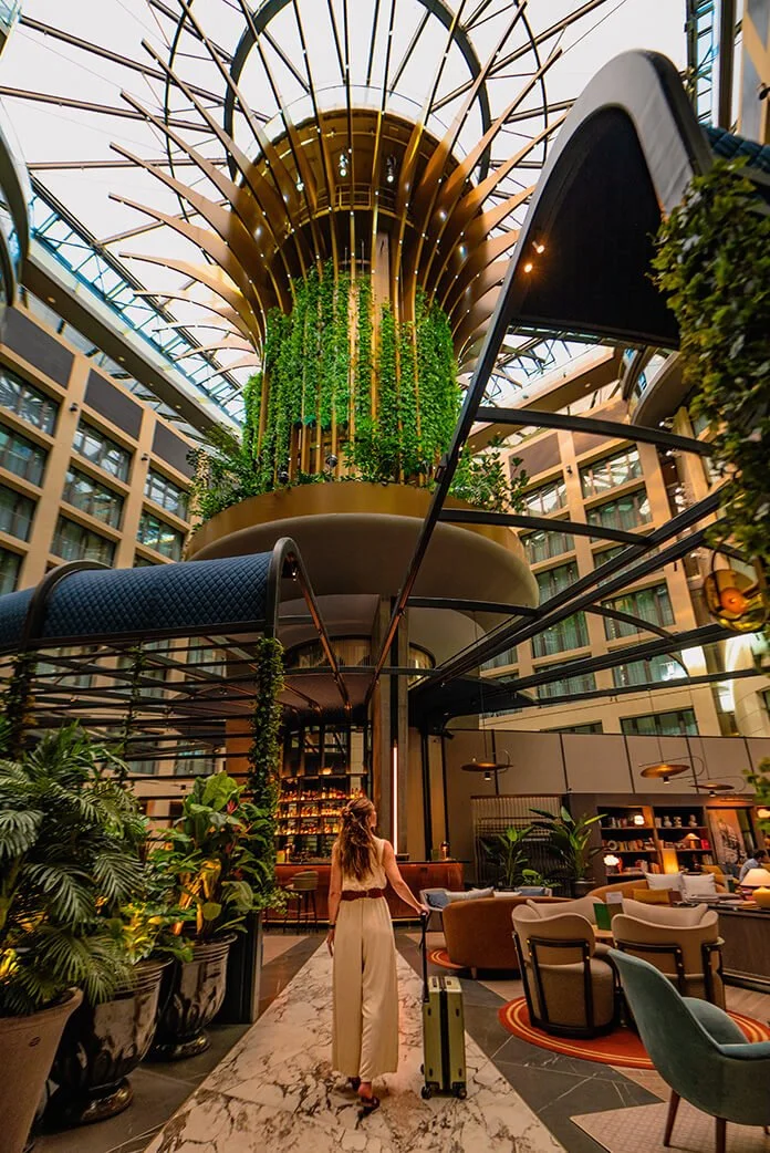Interior of a modern hotel lobby with a tall vertical garden, a spiral staircase, and stylish seating areas.
