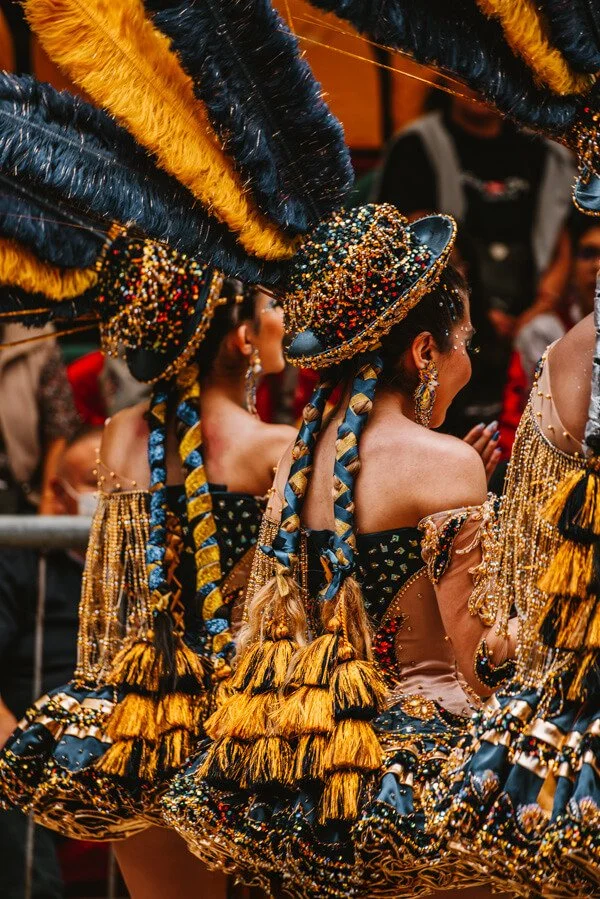 Women in colorful, beaded, and feathered costumes participating in a cultural parade or festival. Oruro carnival in Bolivia.