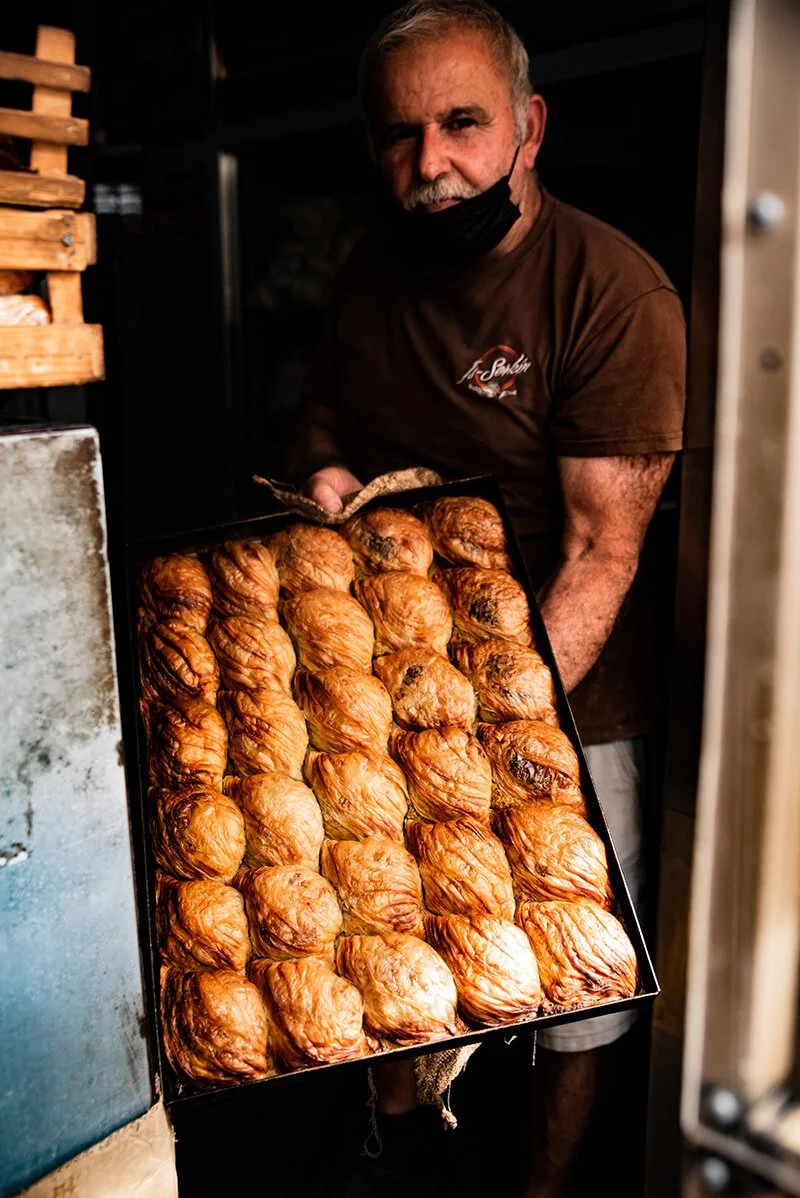A man wearing a brown shirt and black face mask holding a tray of cooked baked potatoes. Street photography in Malta.