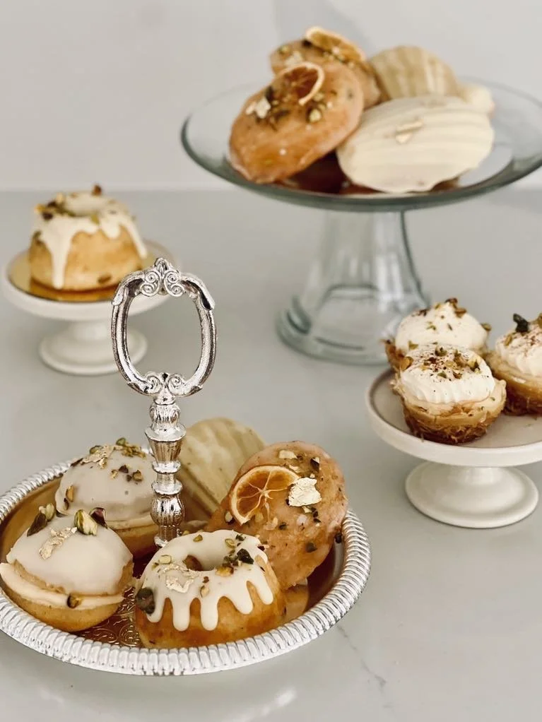 Assorted glazed and decorated donuts on silver, glass, and white cake stands.