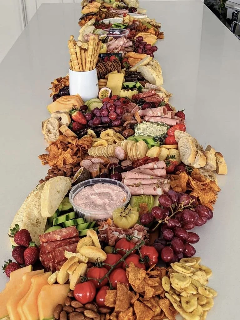 A long table filled with a variety of cheeses, fruits, crackers, meats, and dips arranged in an elaborate charcuterie spread.