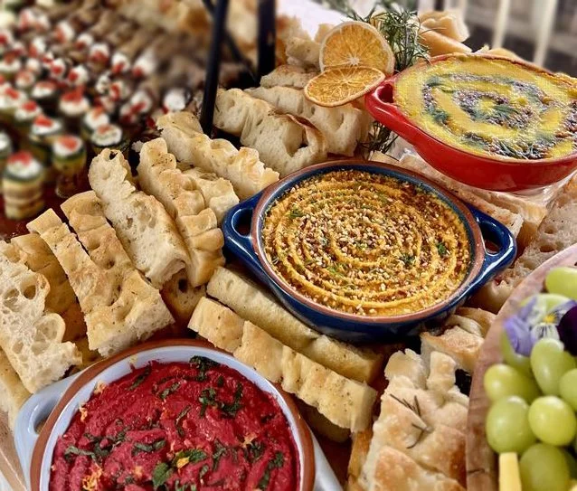 Assorted Mediterranean appetizers including hummus, baba ganoush, bread, grapes, and garnishes on a dinner table.