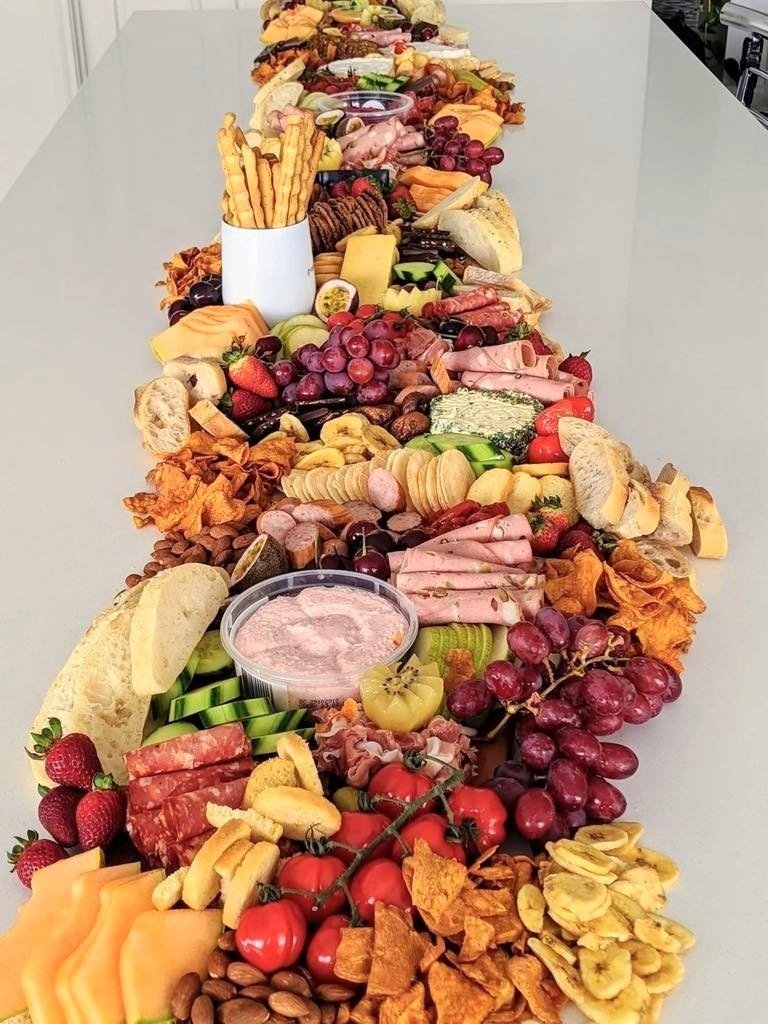 A long table filled with an assortment of cheese, fruits, nuts, crackers, and deli meats for a charcuterie platter.