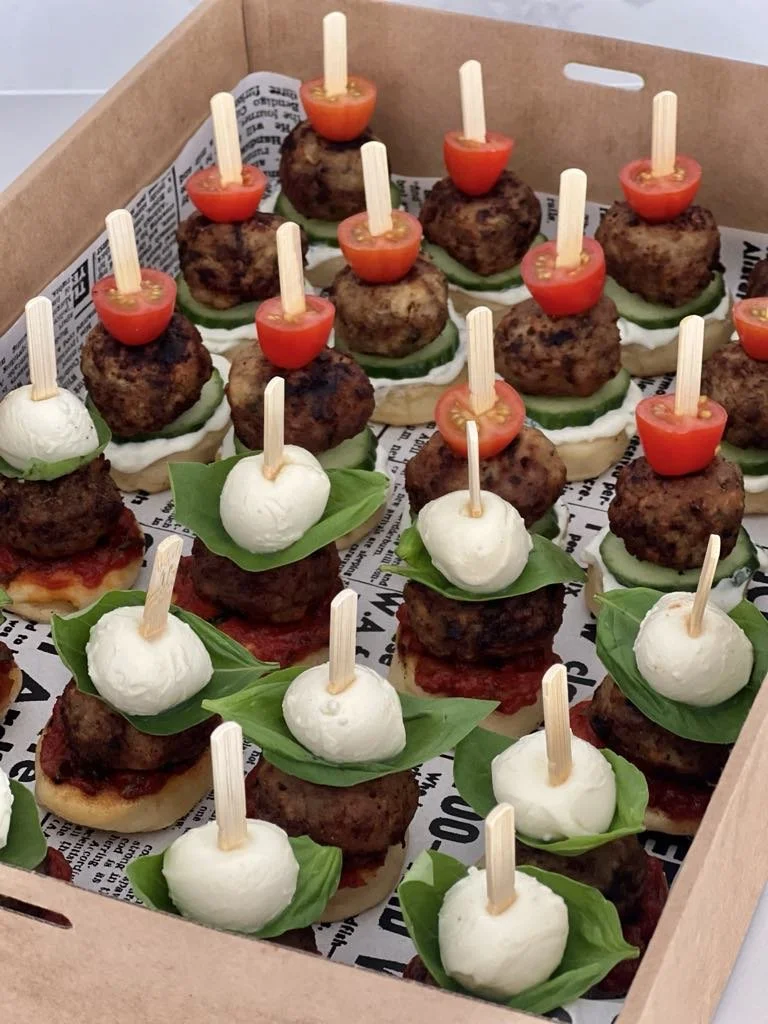 Tray of mini sliders with basil, mozzarella balls, cherry tomatoes, and meatballs