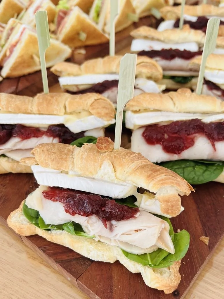 Close-up of chicken sandwiches on croissants with lettuce and cranberry sauce, served on a wooden board.
