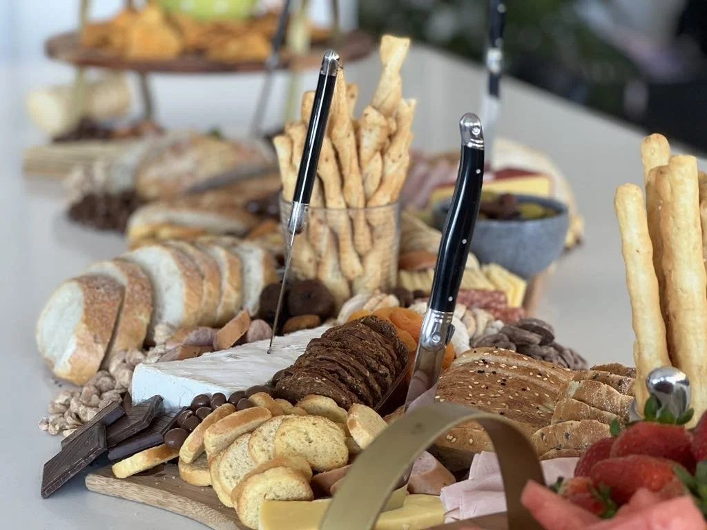 A large cheese and charcuterie board with bread, crackers, dips, and assorted snacks, including strawberries and breadsticks.